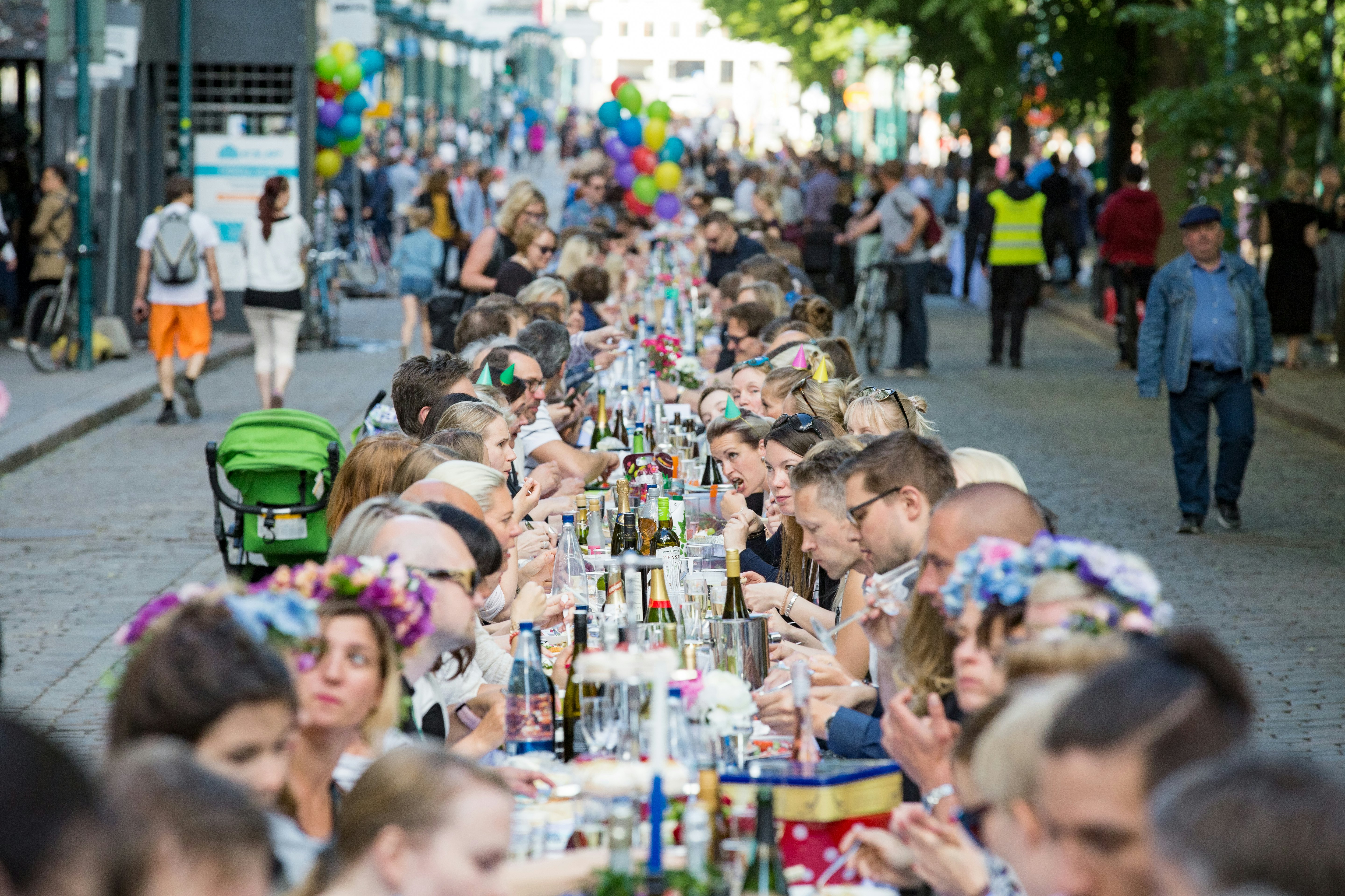 A group of people sit at a long table in a moment of communal dining on a city street.