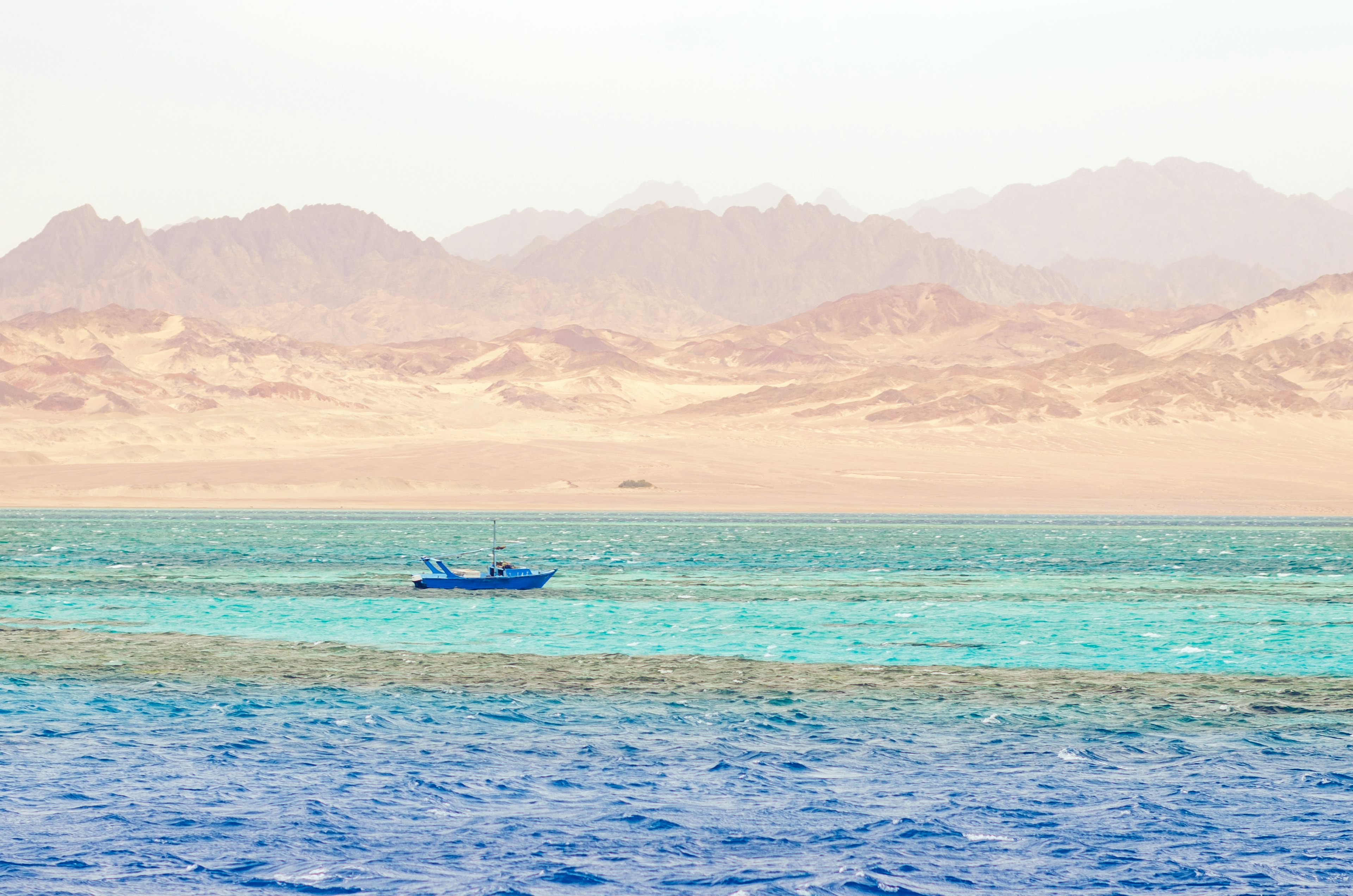 A small blue boat in turquoise water; an arid, mountainous landscape is on the far shore.