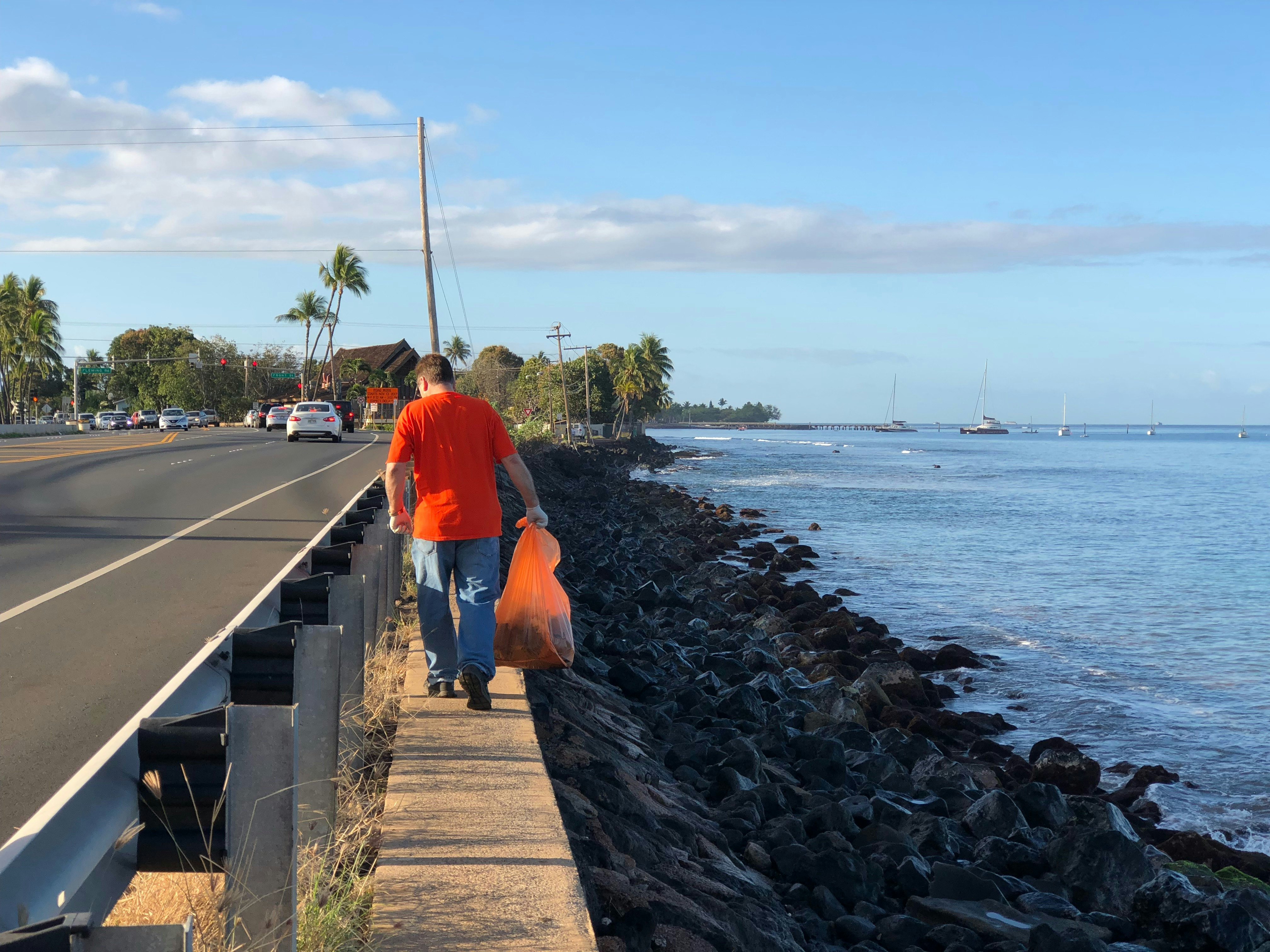 Highway cleanup volunteer looking for trash to pick up next to the beach in Lahaina, Maui