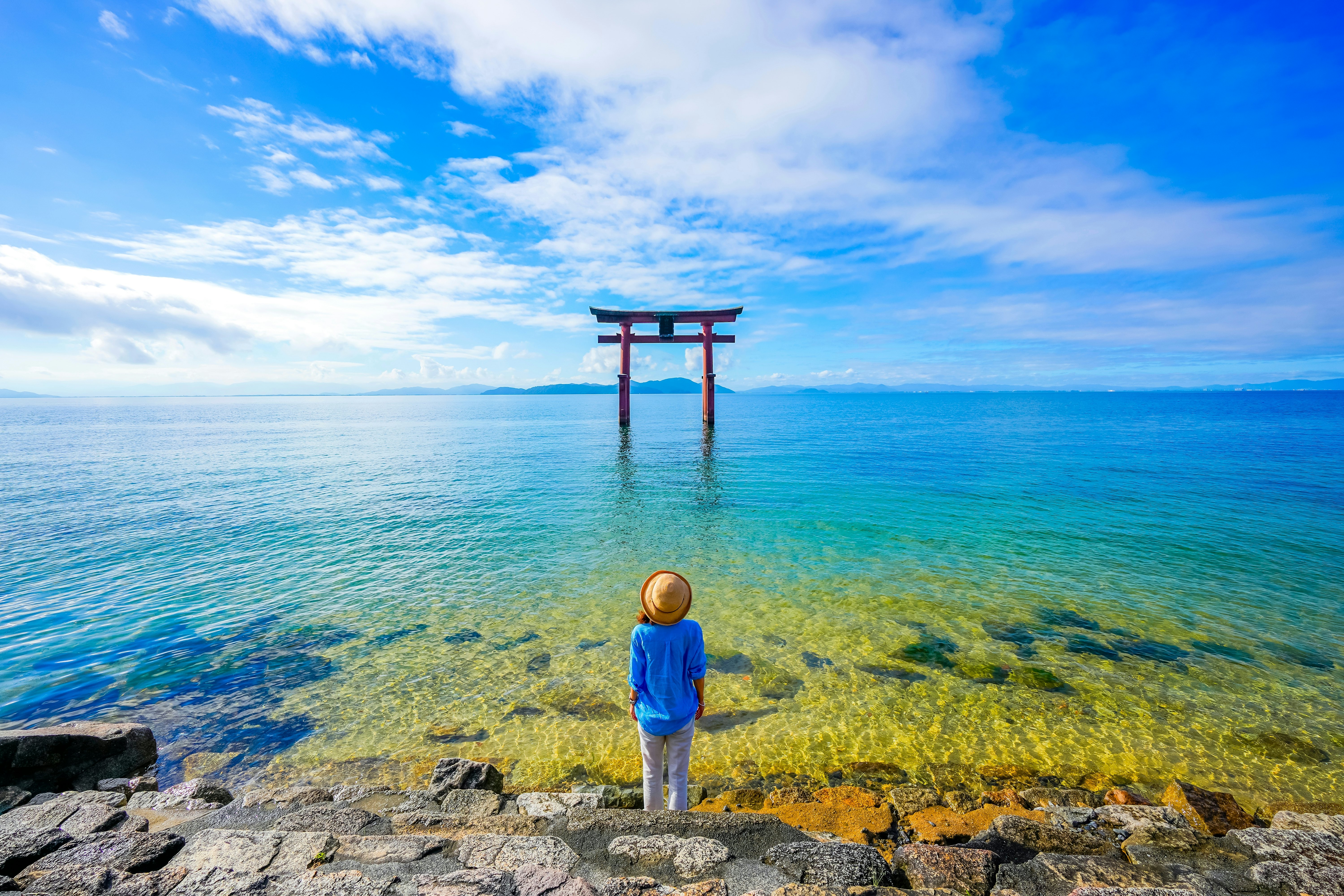 Woman on shores of Lake Biwa gazing at Torii gate, Shiga Prefecture, Japan