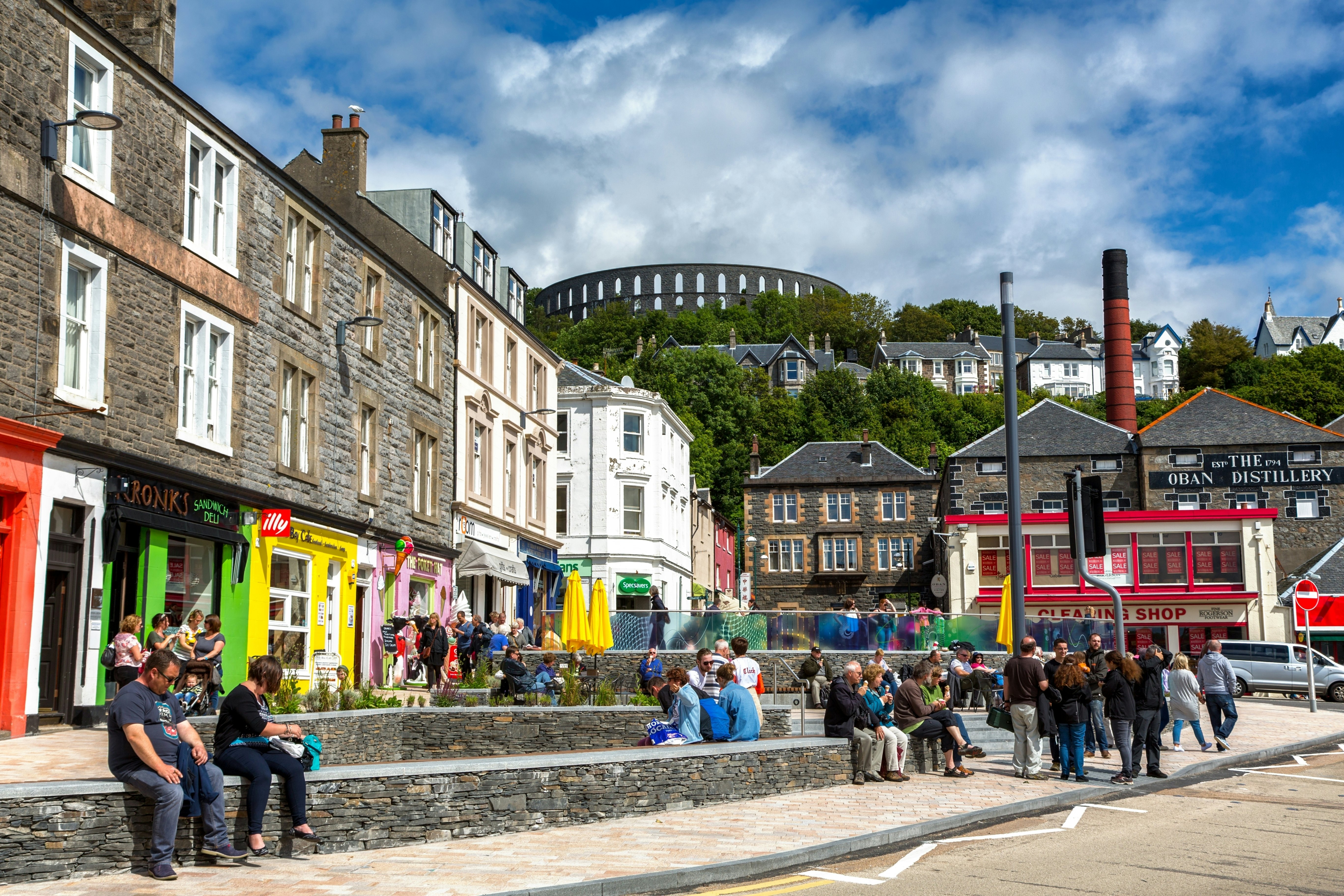 The colourful waterfront shops and cafes of Oban, Scotland, in front of the Oban Distillery and the McCaig Tower.