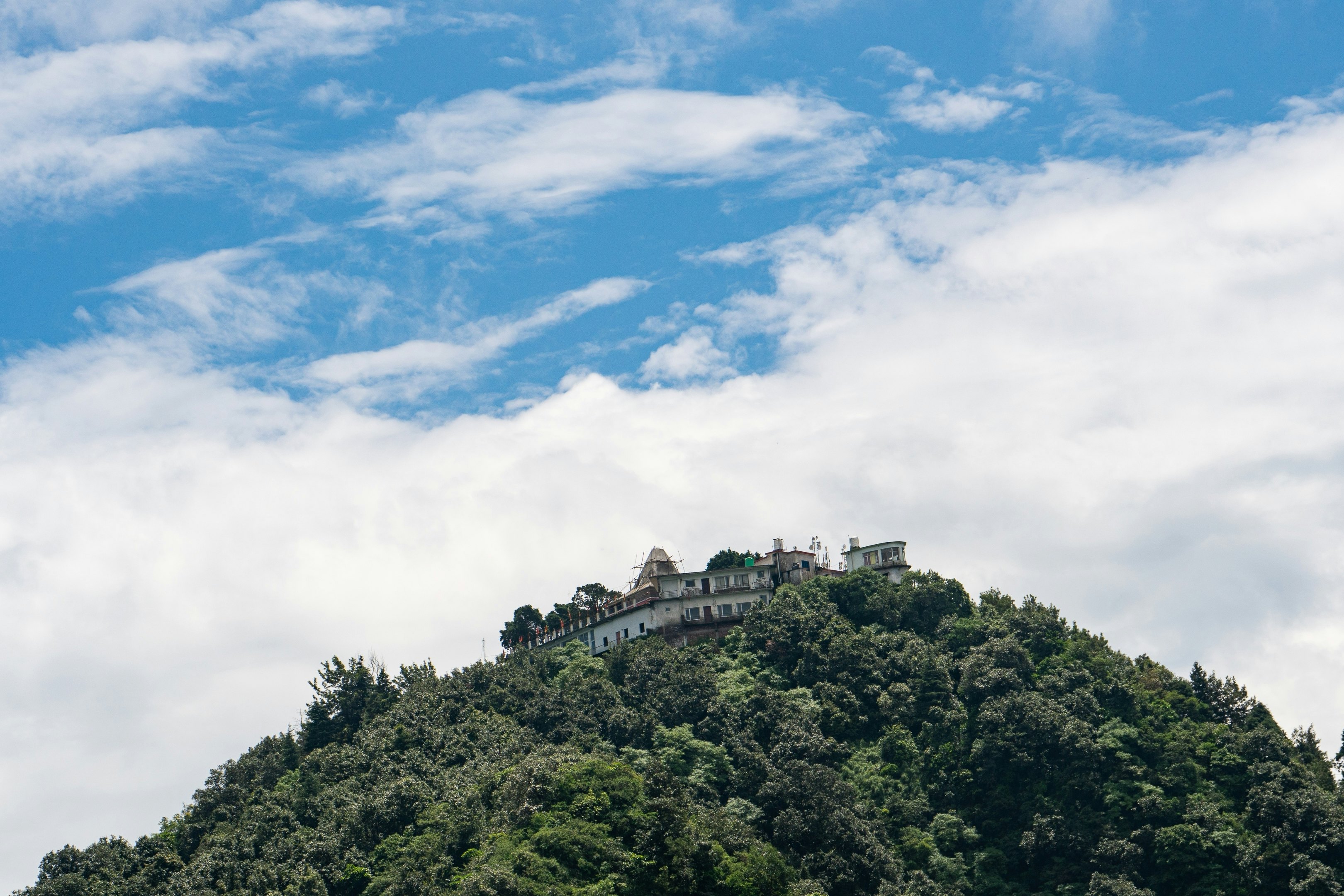 Temple on a forested mountain surrounded by a blue and cloud-filled sky.