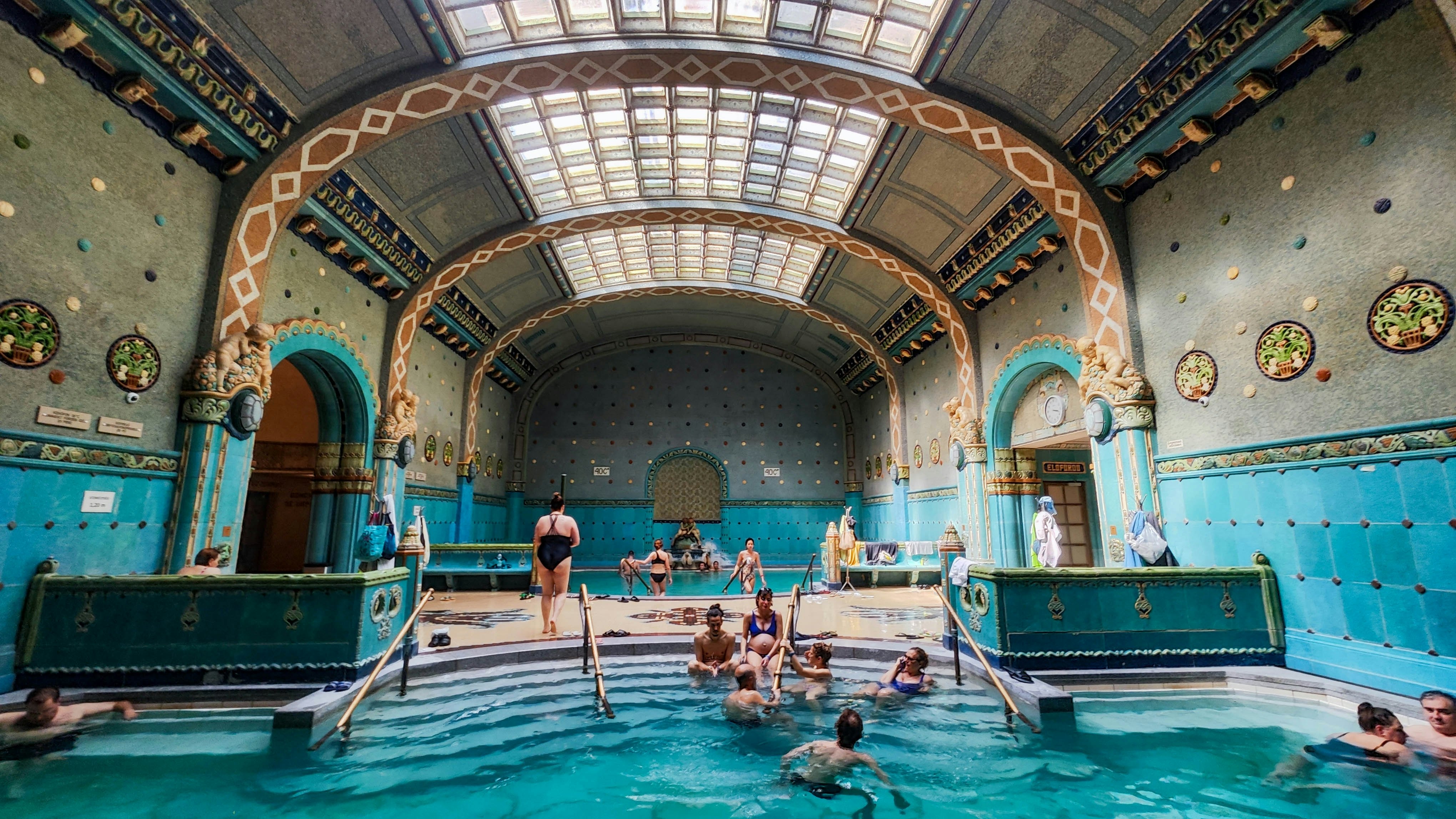 People sitting in an indoor pool with ornate art nouveau decoration over the walls and ceiling.
