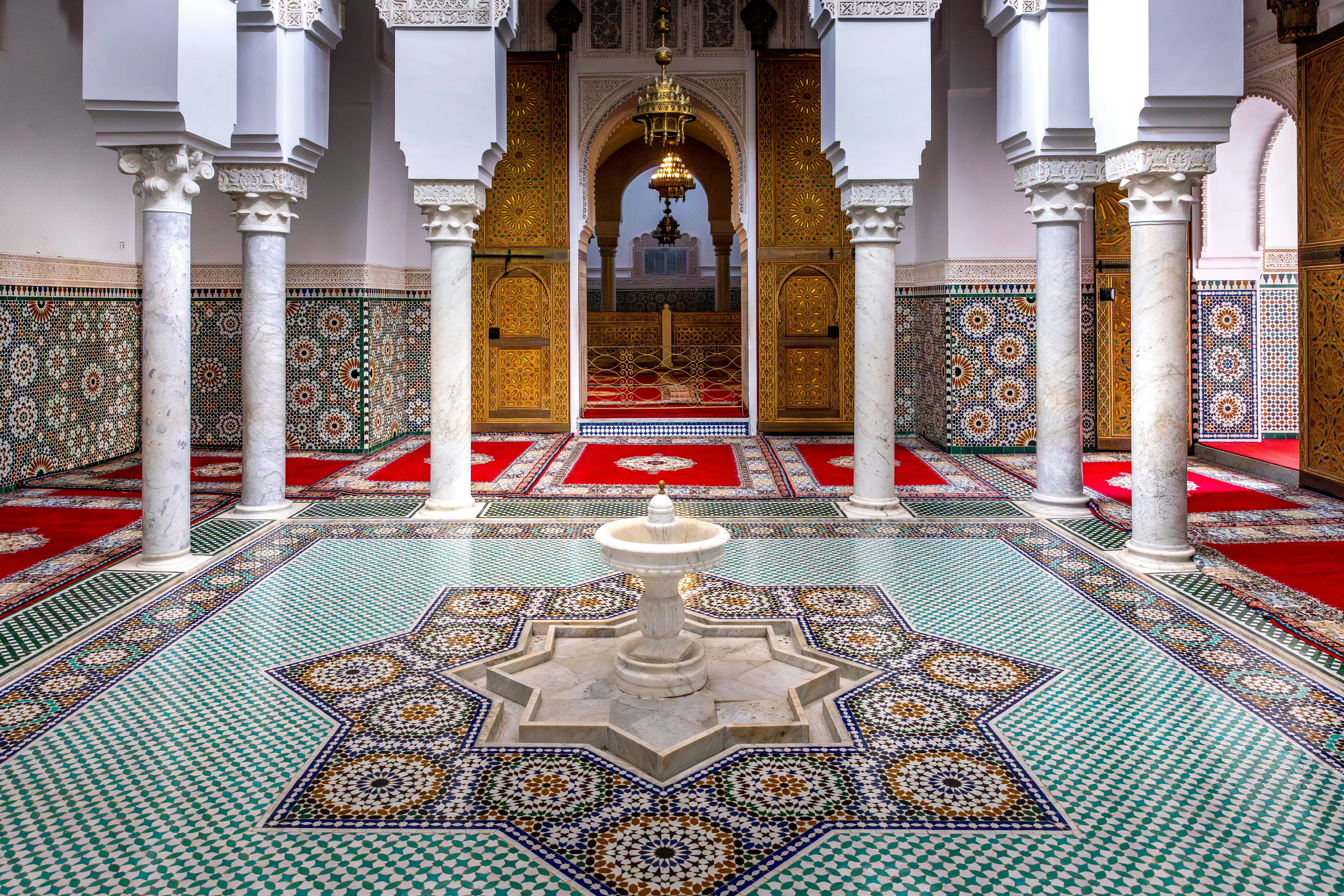 A fountain in the center of a courtyard in Morocco; the floor and walls are covered in spectacular tile patterns.