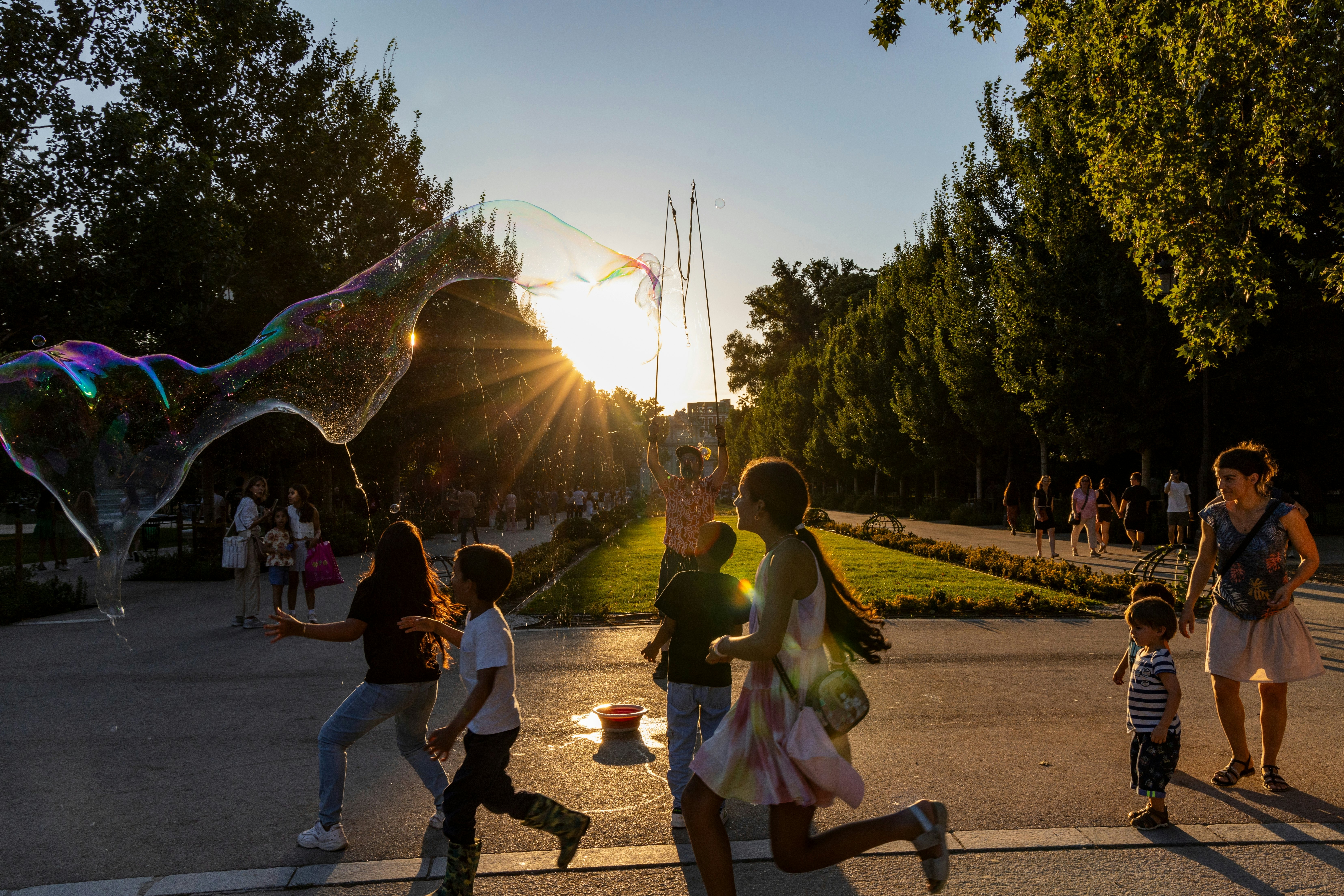 Children at sunset chase the soap bubbles of a street artist in a park in Madrid