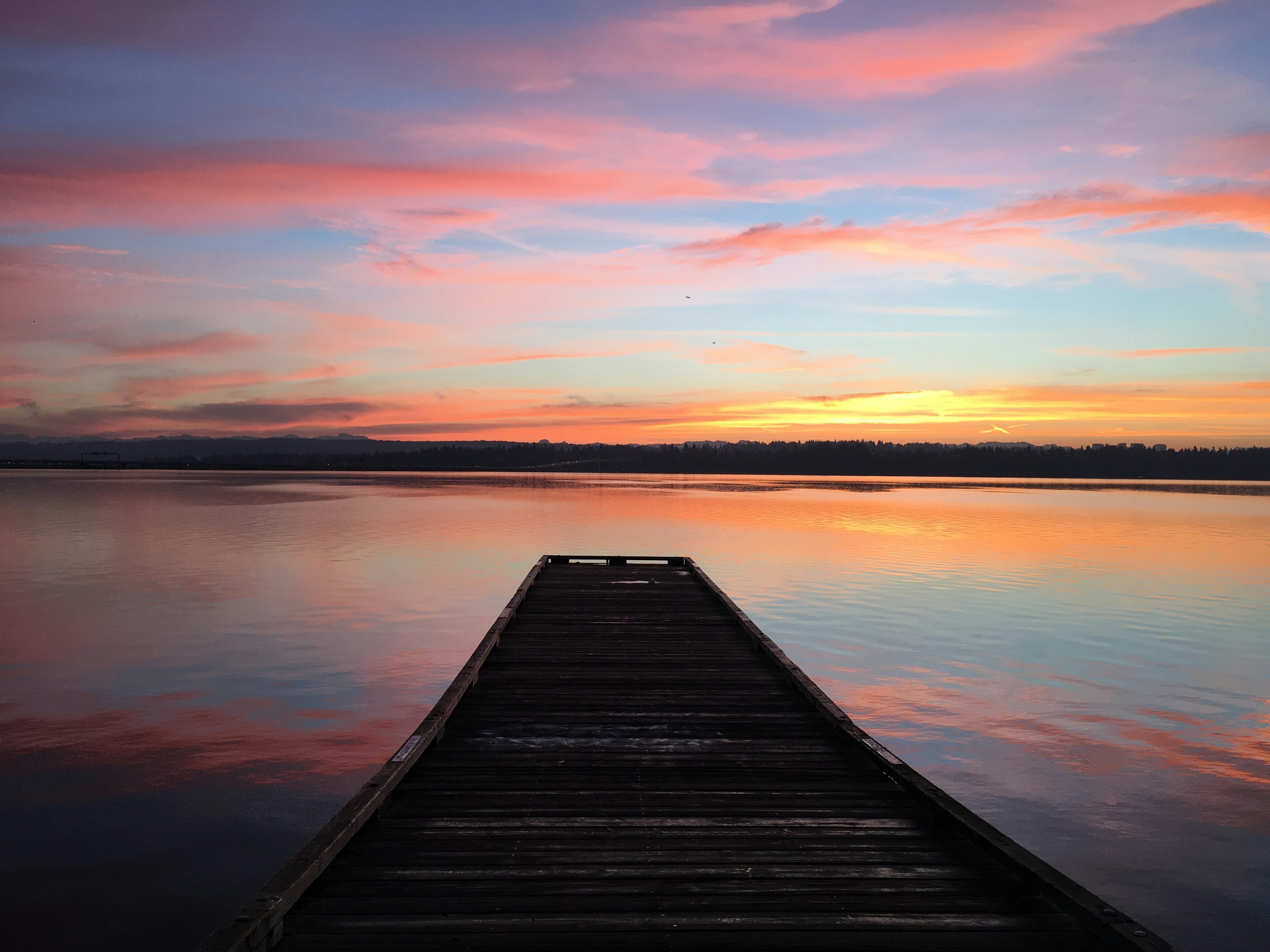 A small wooden pontoon in a lake as the sky turns orange at sunrise.