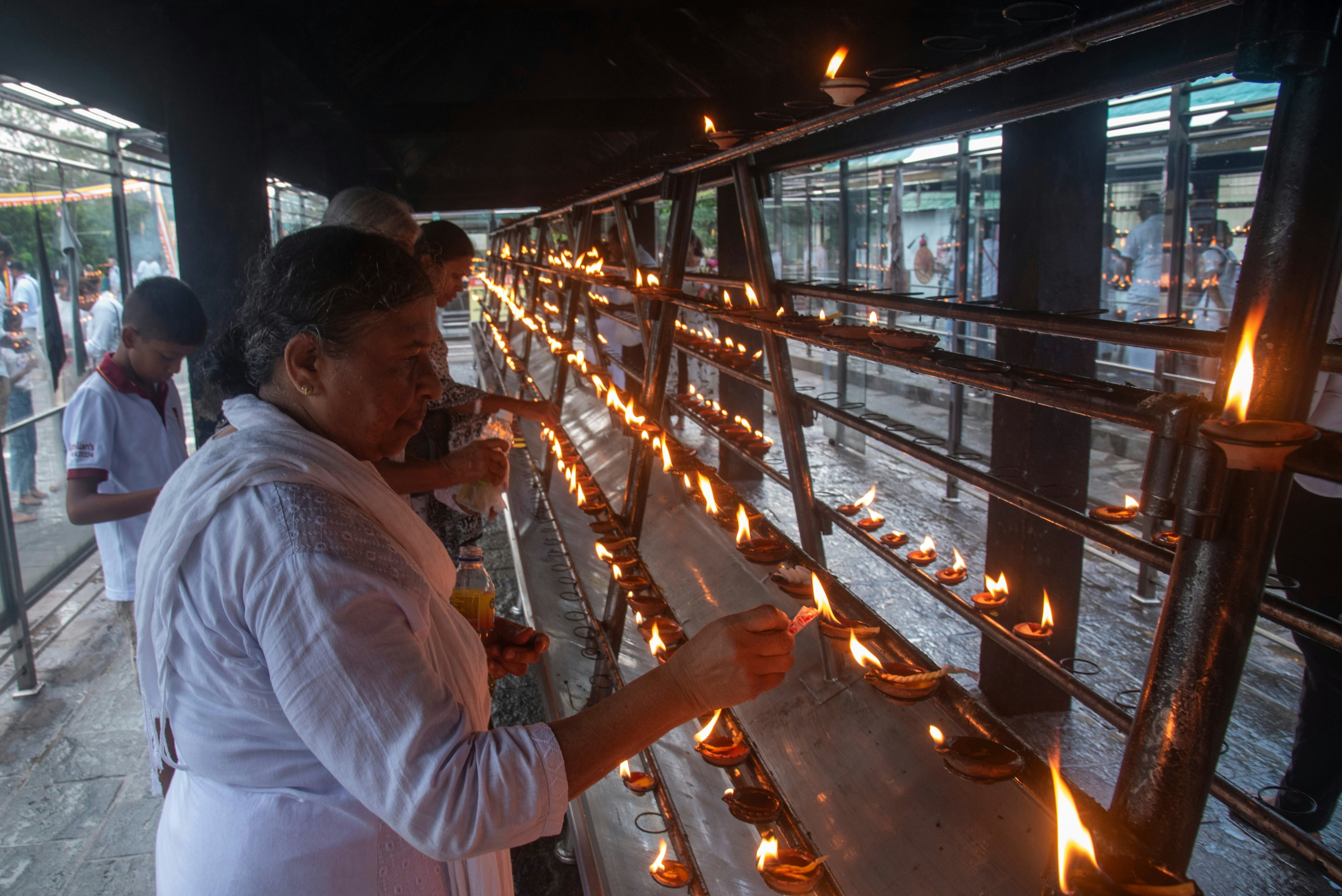 A man dressed in white lights a candle at a shrine.