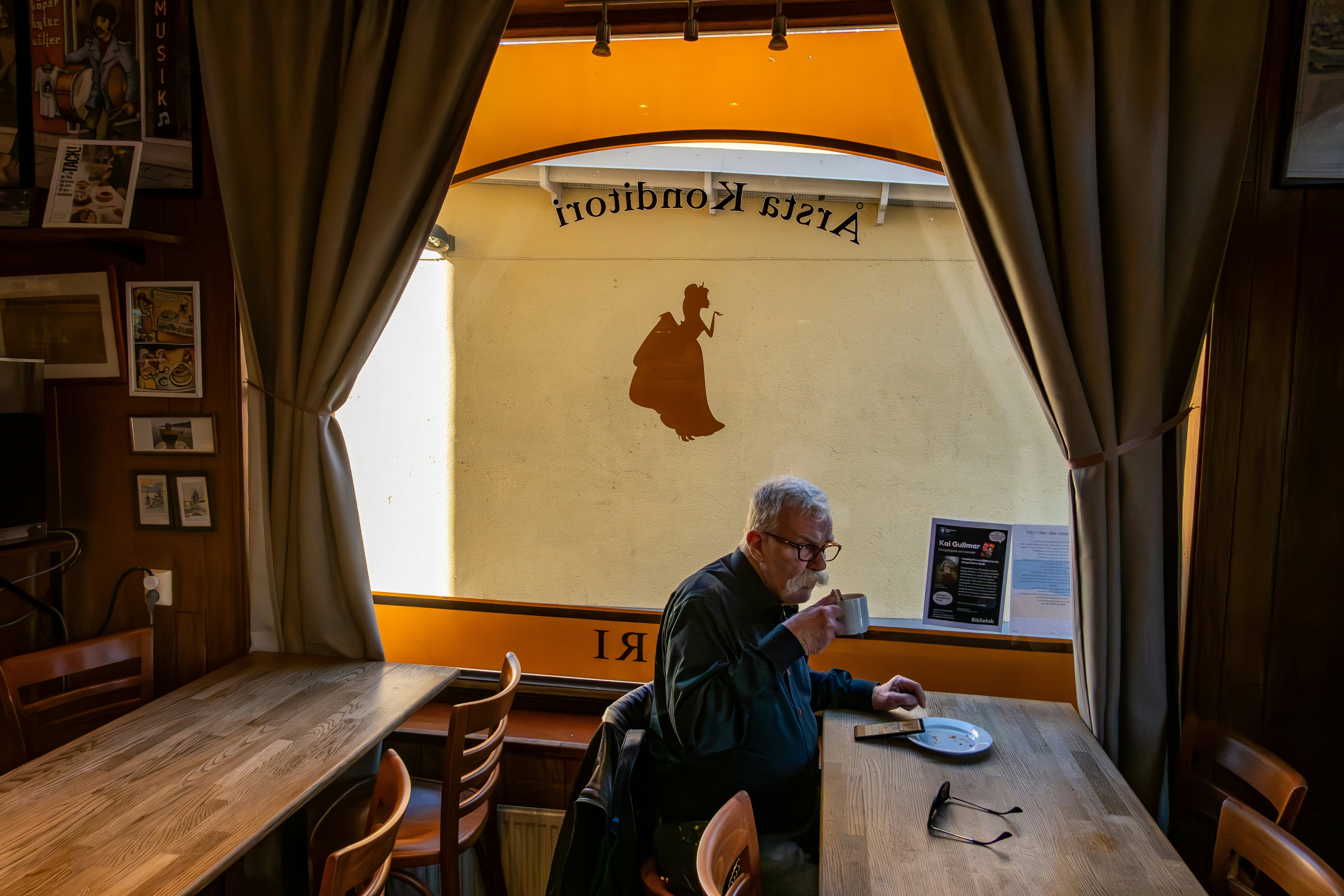 An elderly man sips a cup of coffee at a table in a cafe.