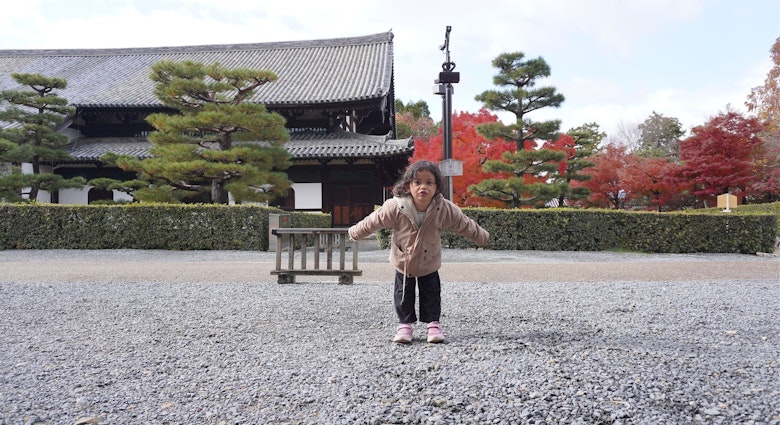 A young girl poses playfully in front of a traditional Japanese temple surrounded by beautifully manicured pine trees and vibrant autumn foliage. Captured during fall season in Kyoto, Japan.; Shutterstock ID 2641309481; purchase_order:65050 - Digital Destinations and Articles; job:Lonely Planet Online Editorial; client:Kyoto with kids; other:Brian Healy
2641309481