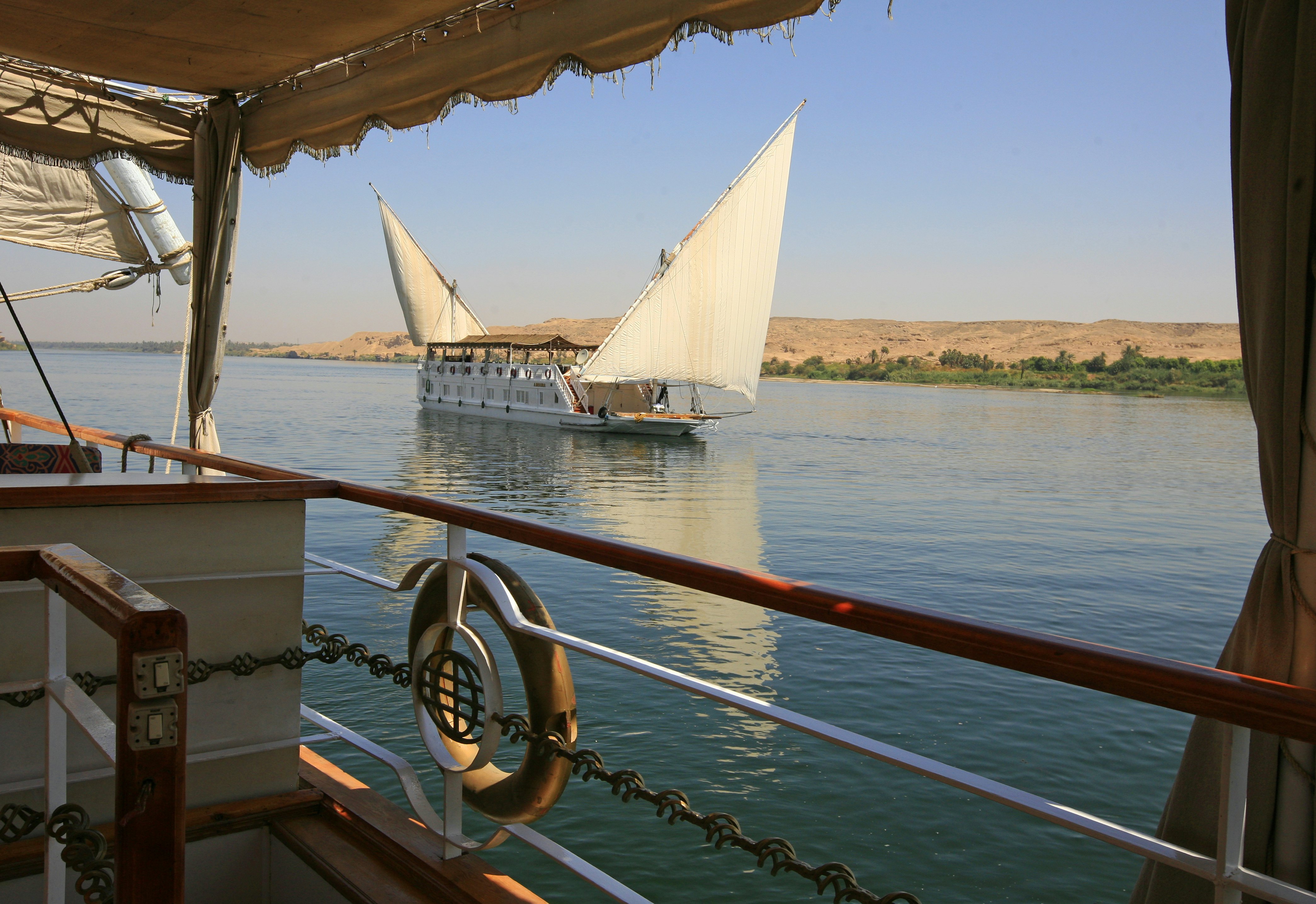 A sailing ship with two large triangular sails on a river.