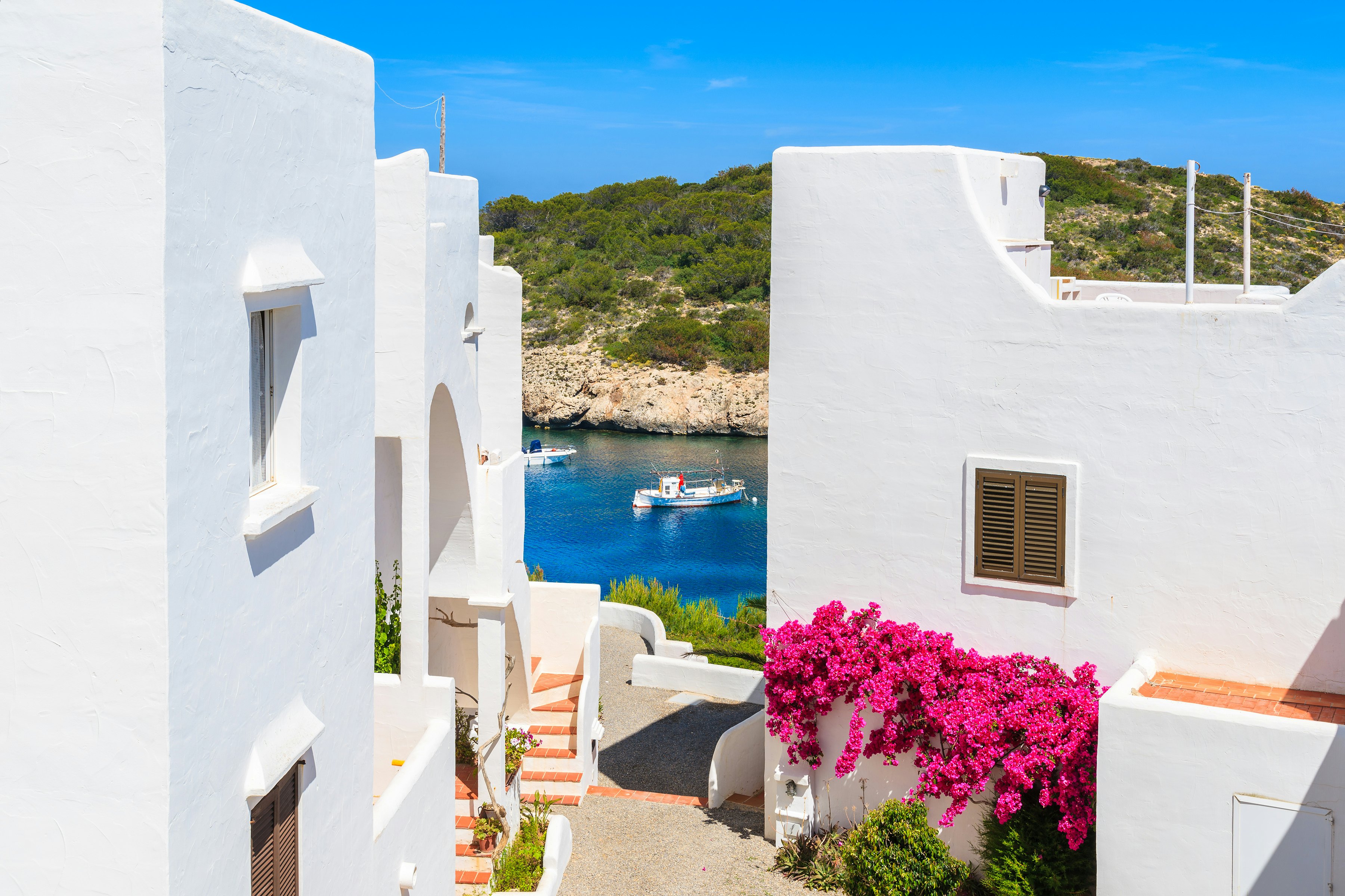 Traditional white houses decorated with flowers and view of fishing boat on sea.