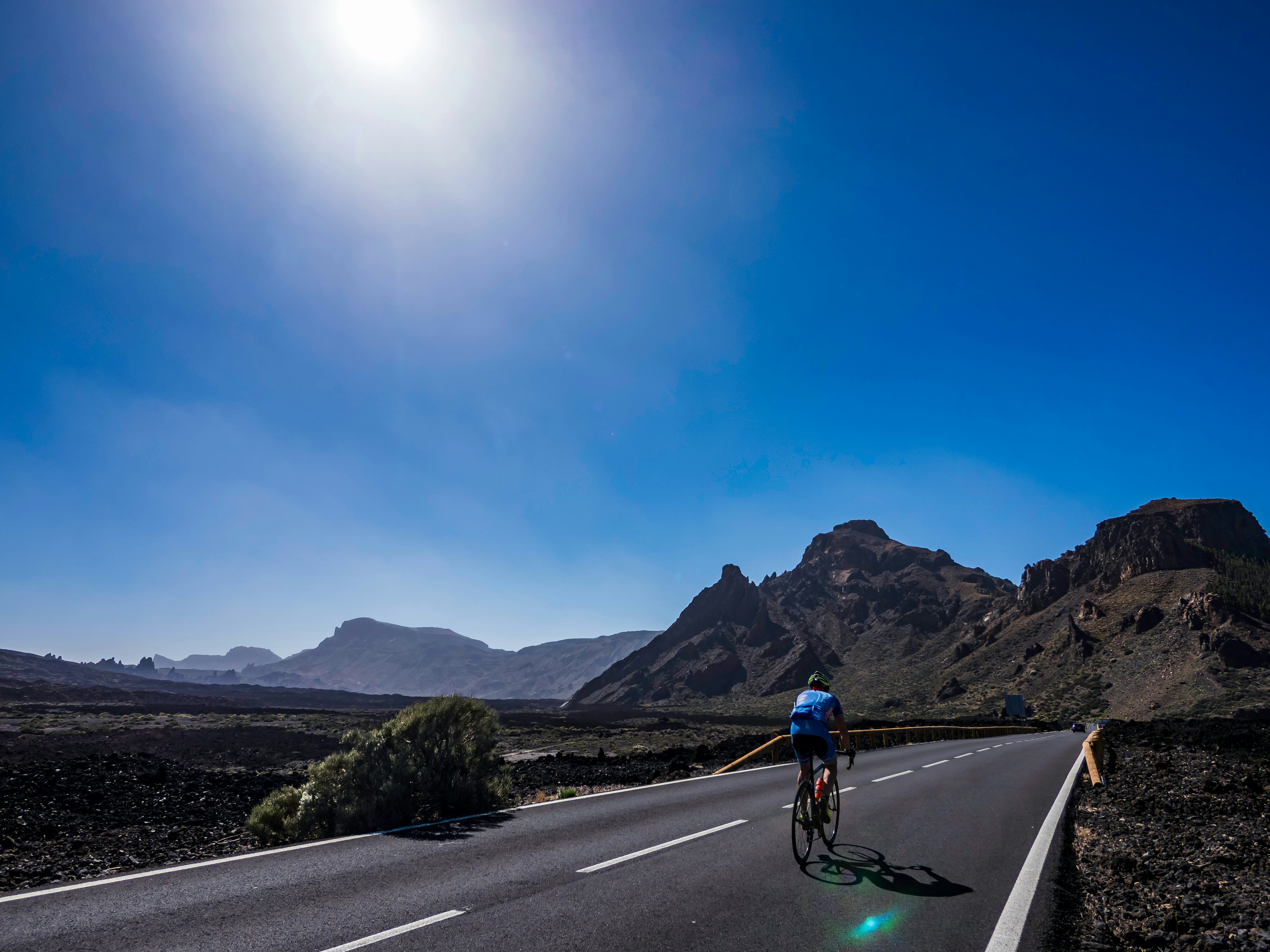 Cyclist riding on a road through a deserted, volcanic landscape in the heat and sunshine