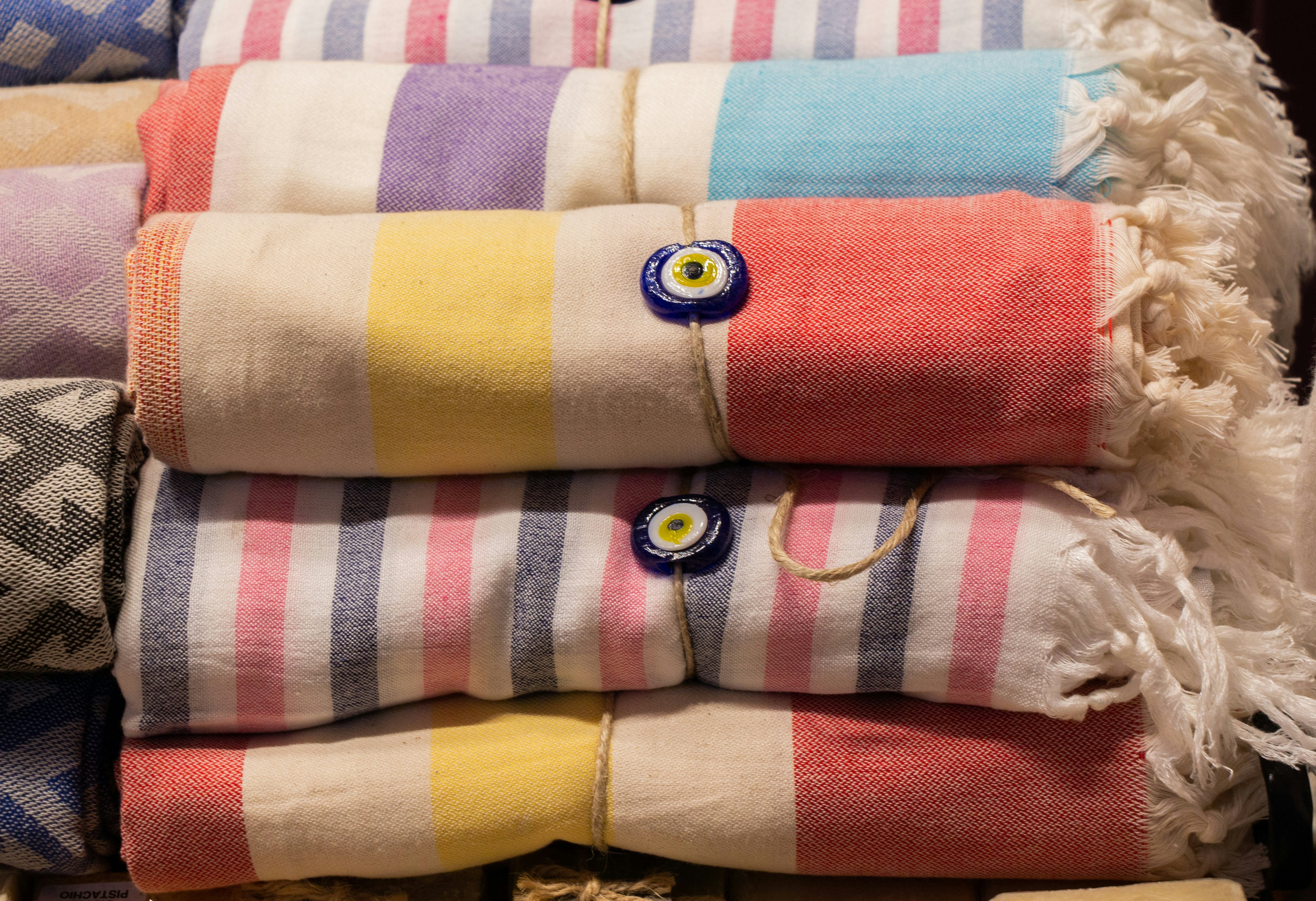 Striped colorful cotton sheets with tassels stacked in a pile at a market stall.