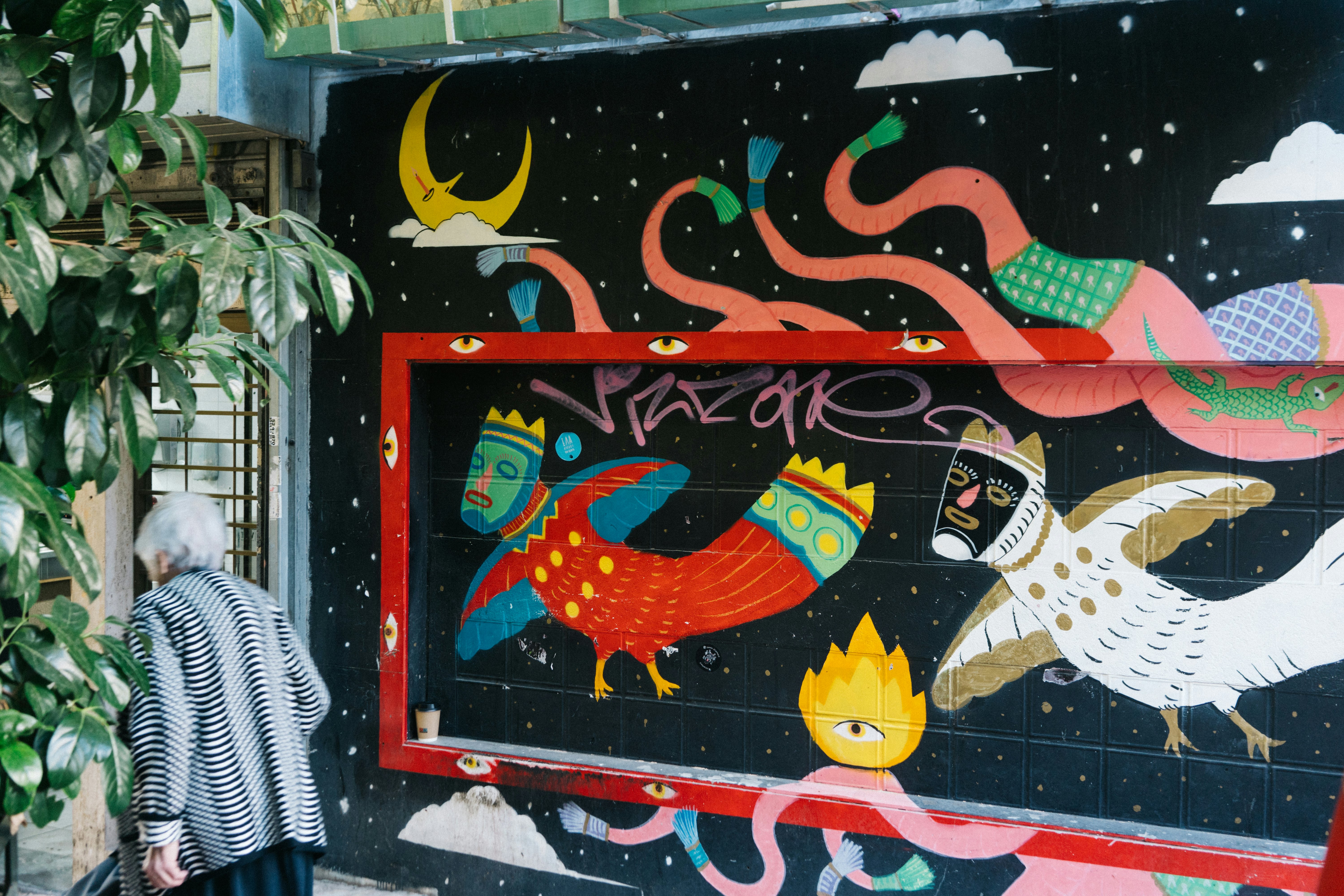 A woman walks past colorful street art painted on the side of a building.