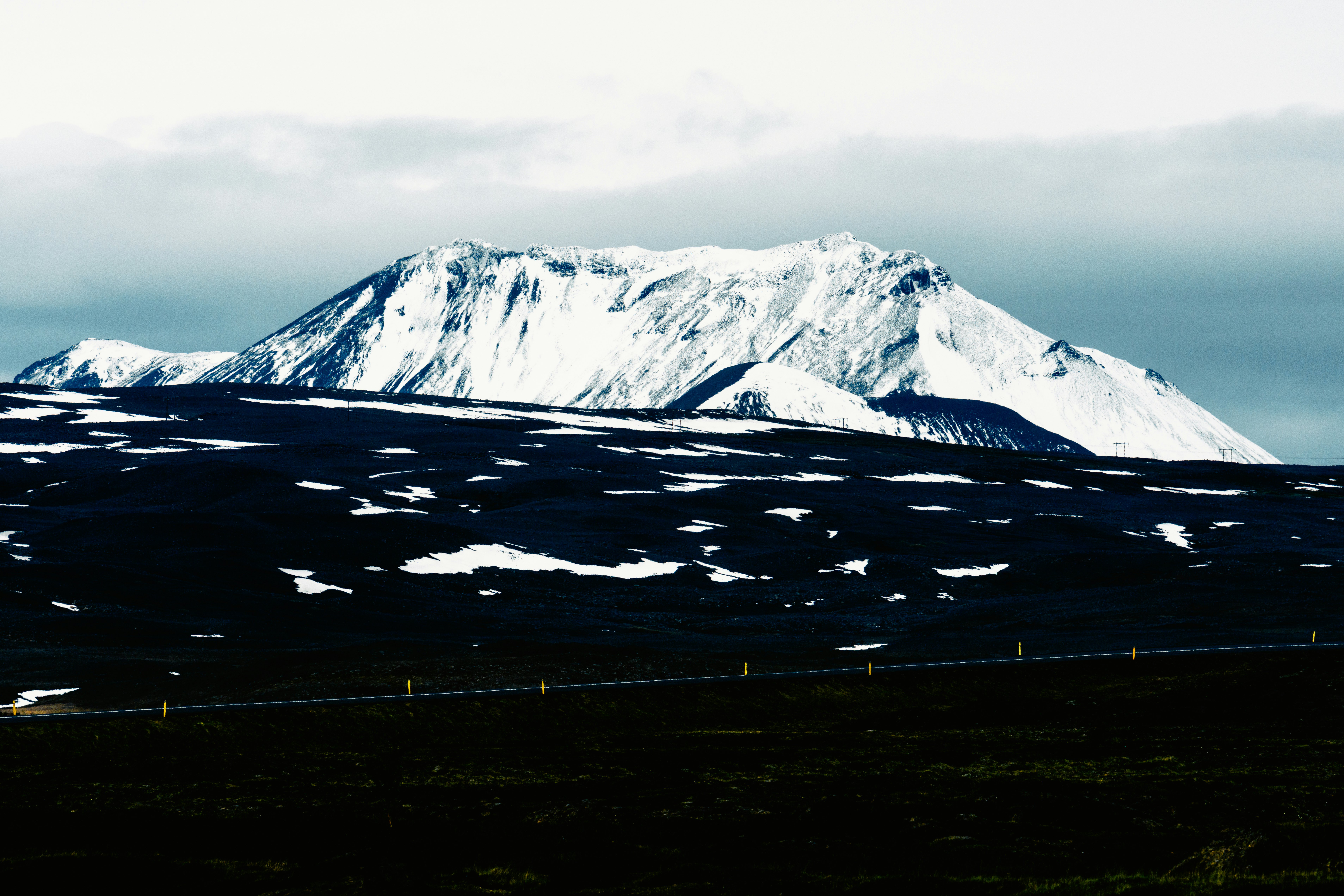 A large icecapped mountain over a black sand landscape