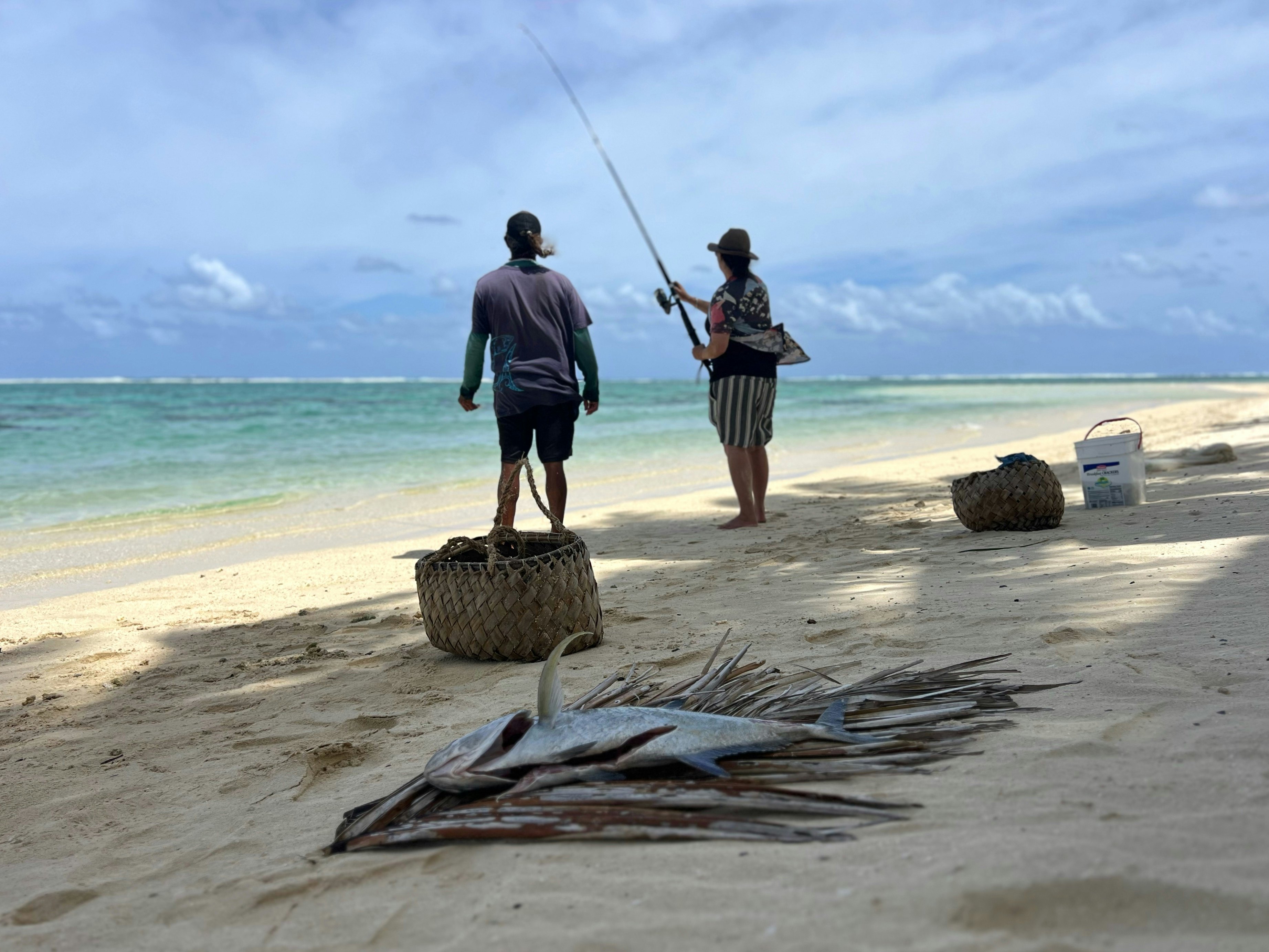 Two people fishing in a lagoon at the edge of a sandy beach.