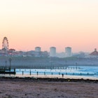 Aberdeen, Scotland, UK - October 9, 2015: A surfer walks on Aberdeen beach at sunset. The city skyline in the background.