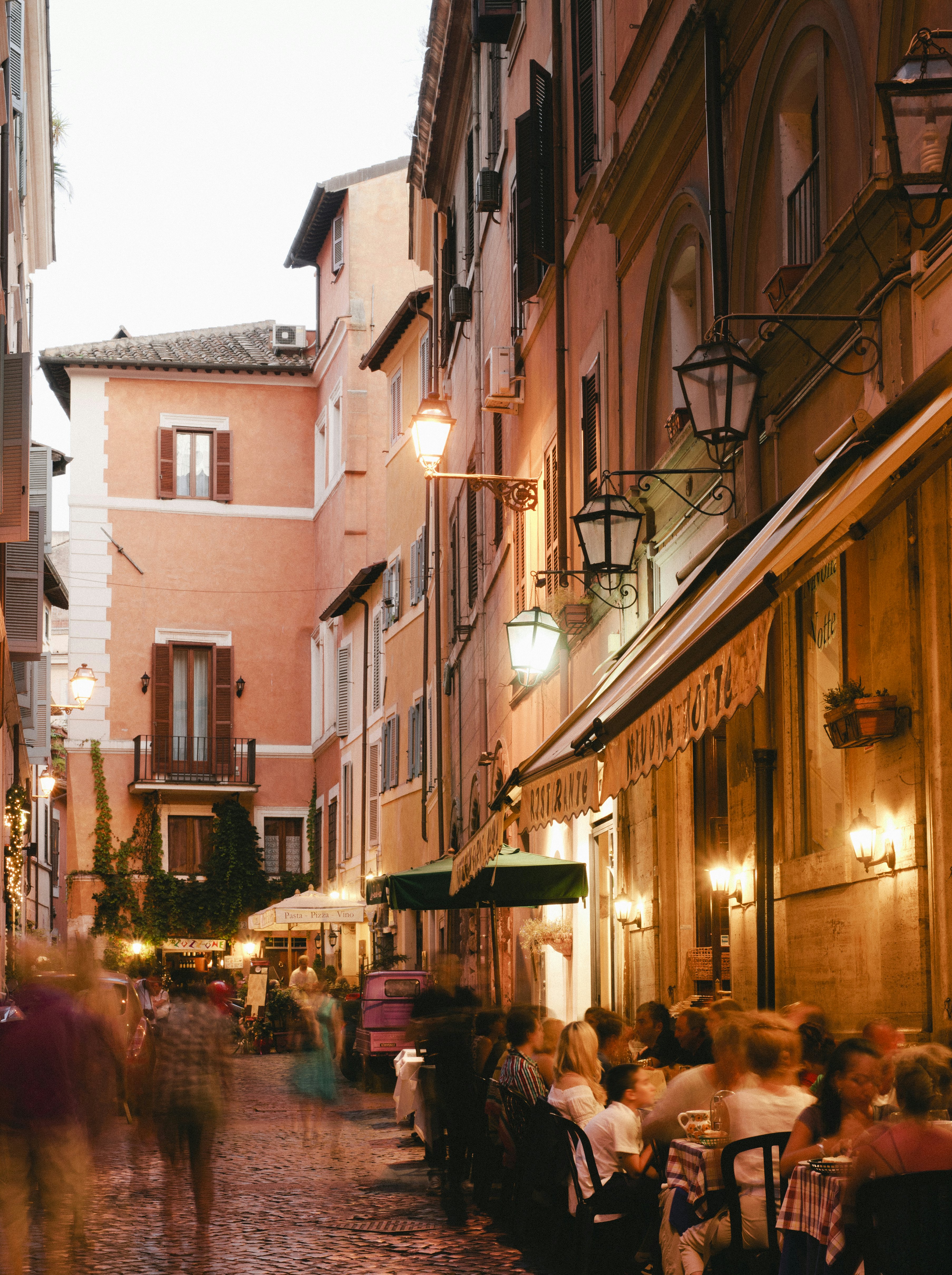 Narrow street in Rome lined with people dining by restaurants at night