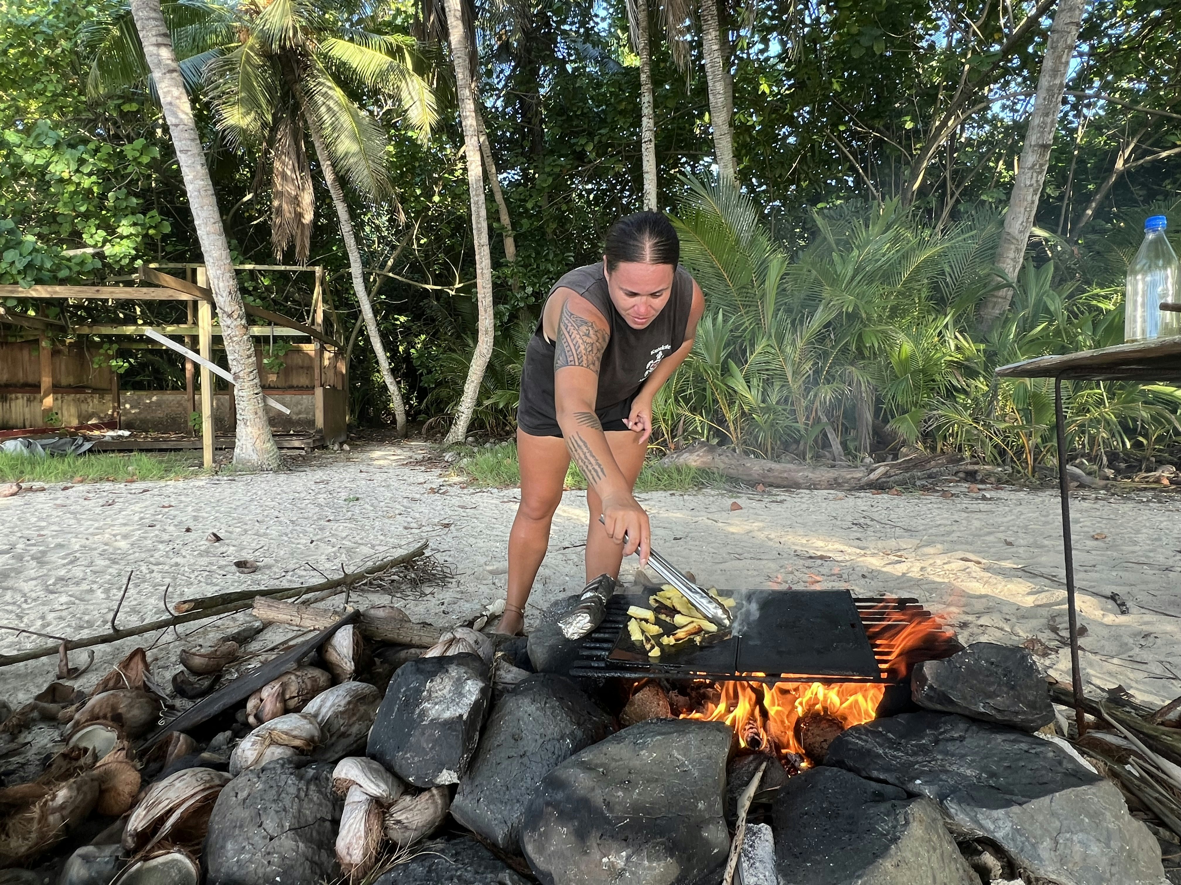 A tour guide prepares a barbecue on a beach lined with palm trees.