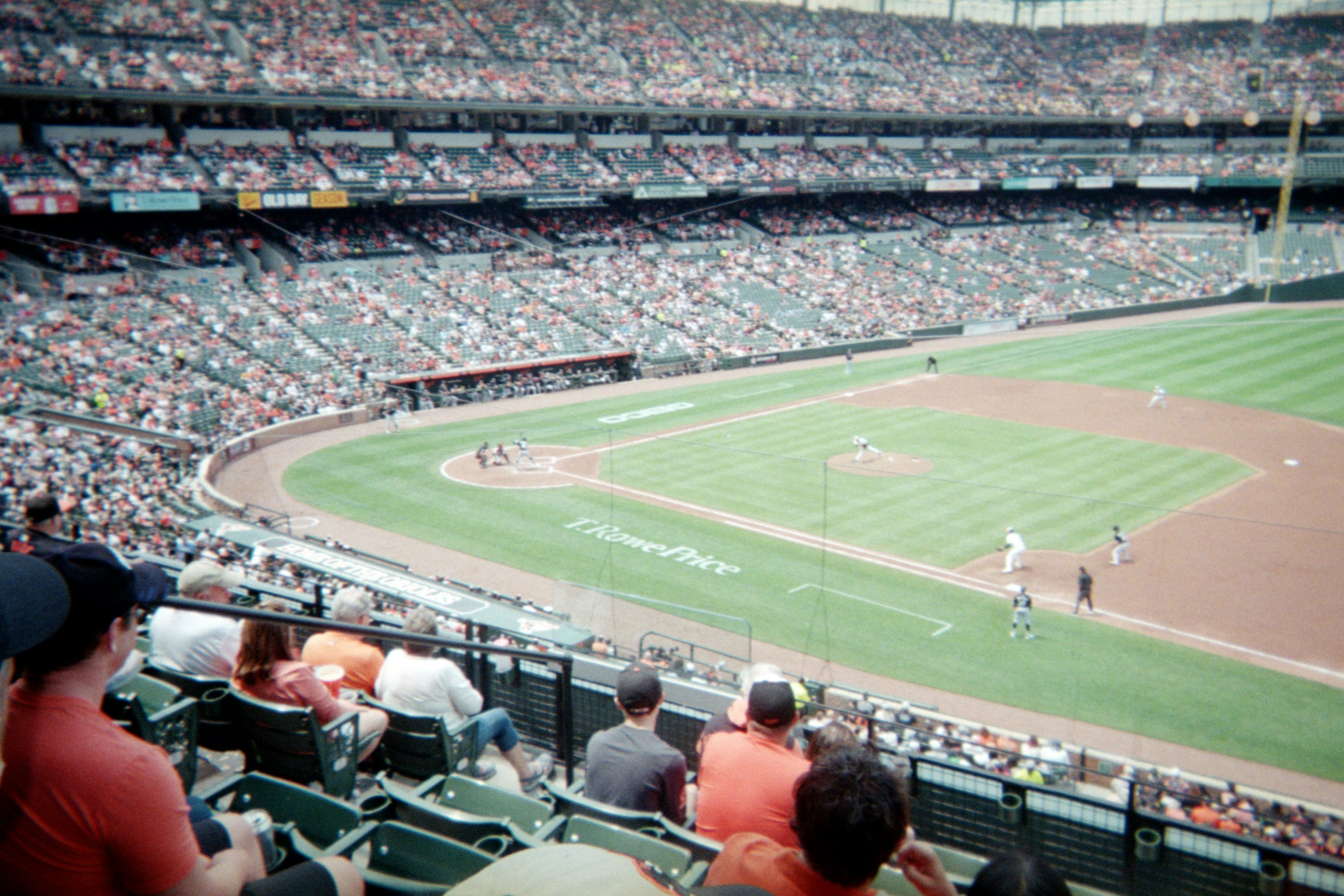 The view of a baseball stadium from the stands with players on the field and fans wearing orange