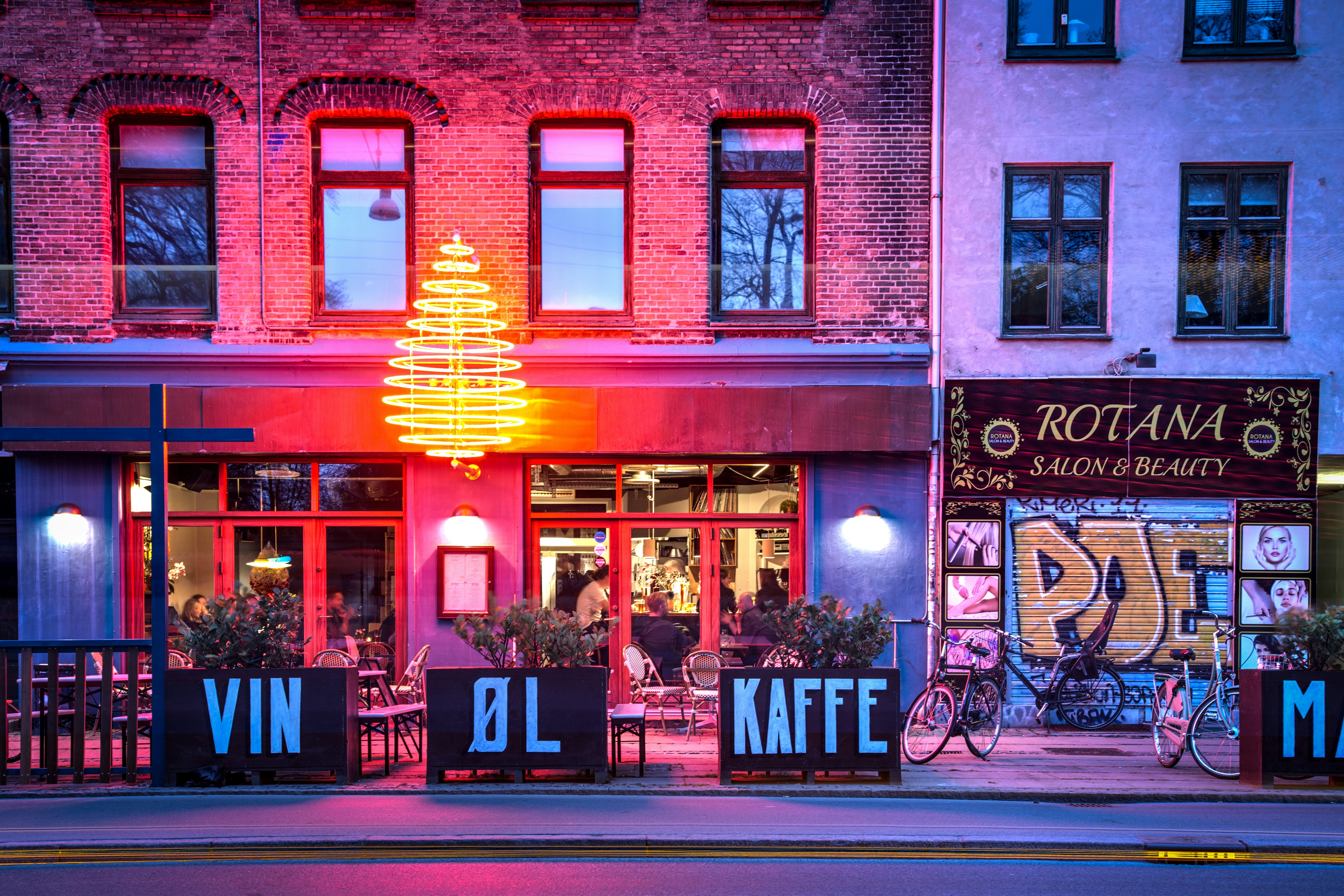 A bar lit upalongside a beauty salone on a city street at night.