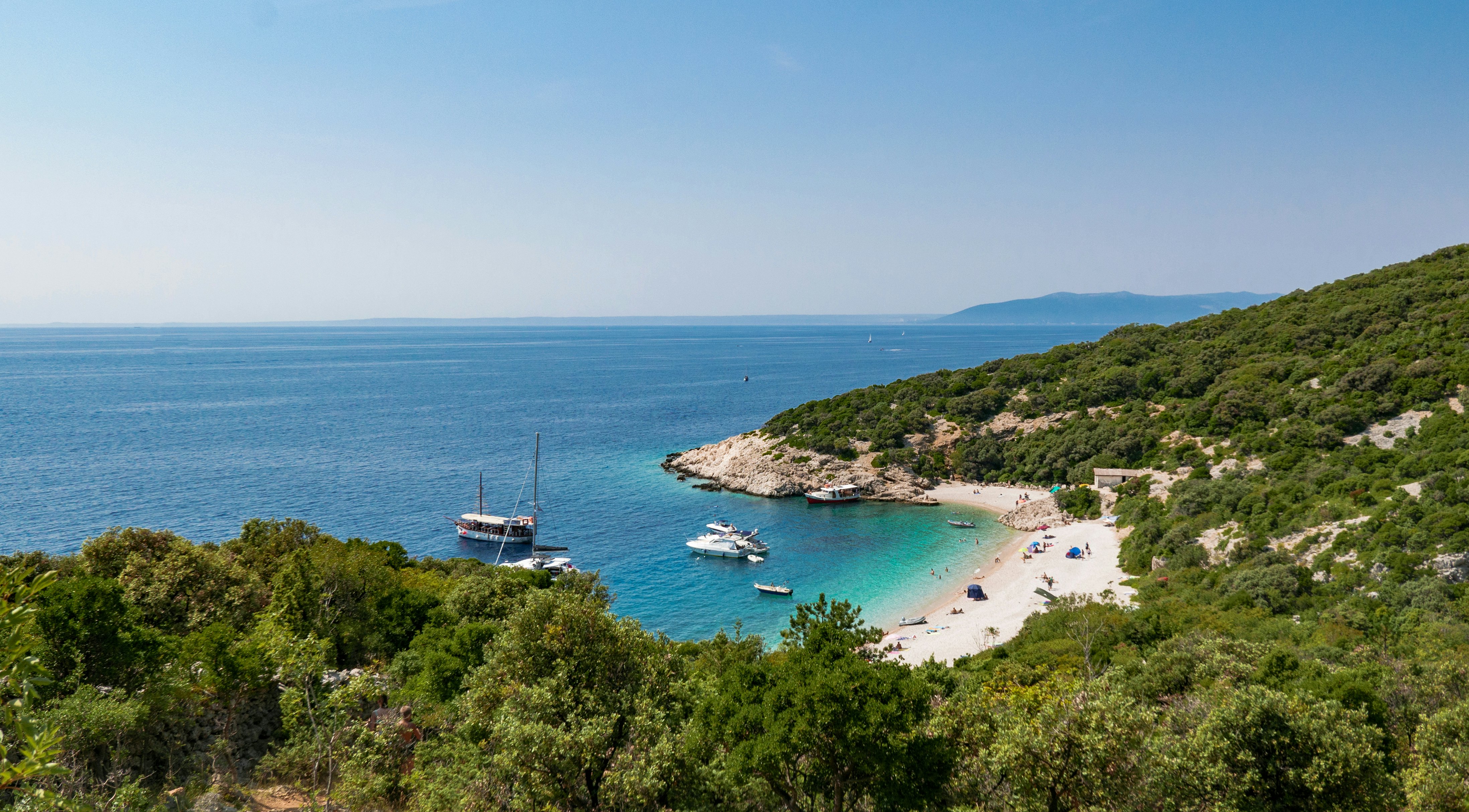 Boats and sunbathers on the beach under Lubenice village on island Cres, Croatia