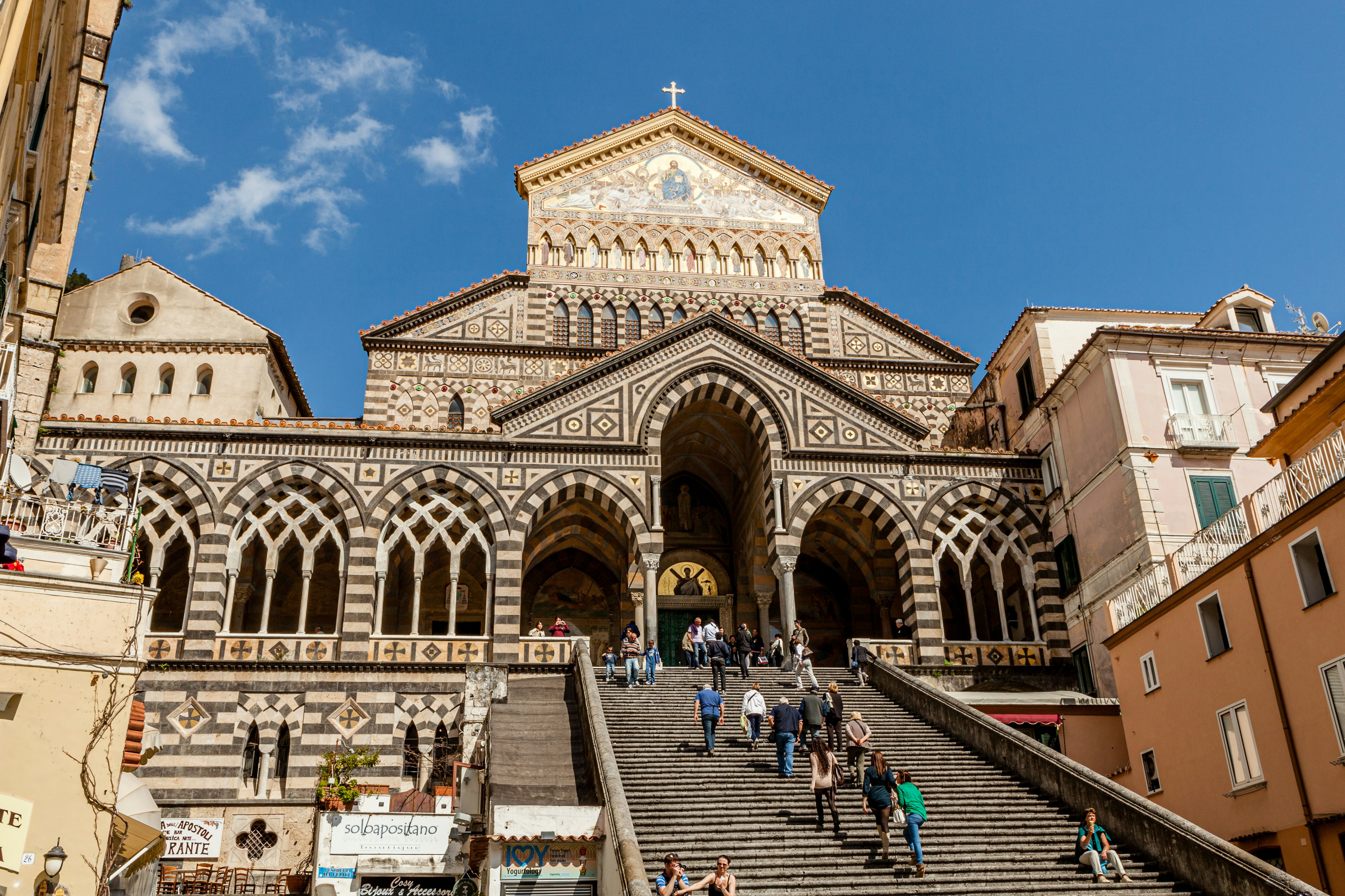 People walking up a steep staircase toward an ornate stone cathedral on a sunny day.