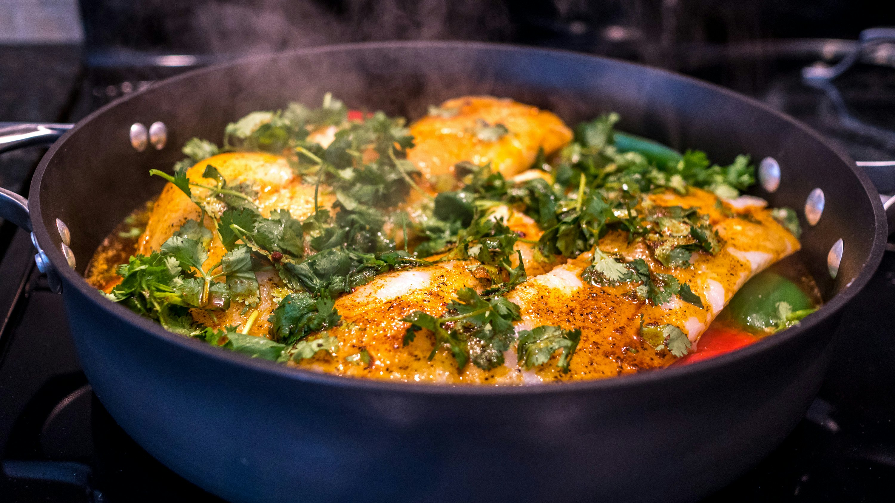 Moroccan fish cooking on the stove with chermoula and pepper.