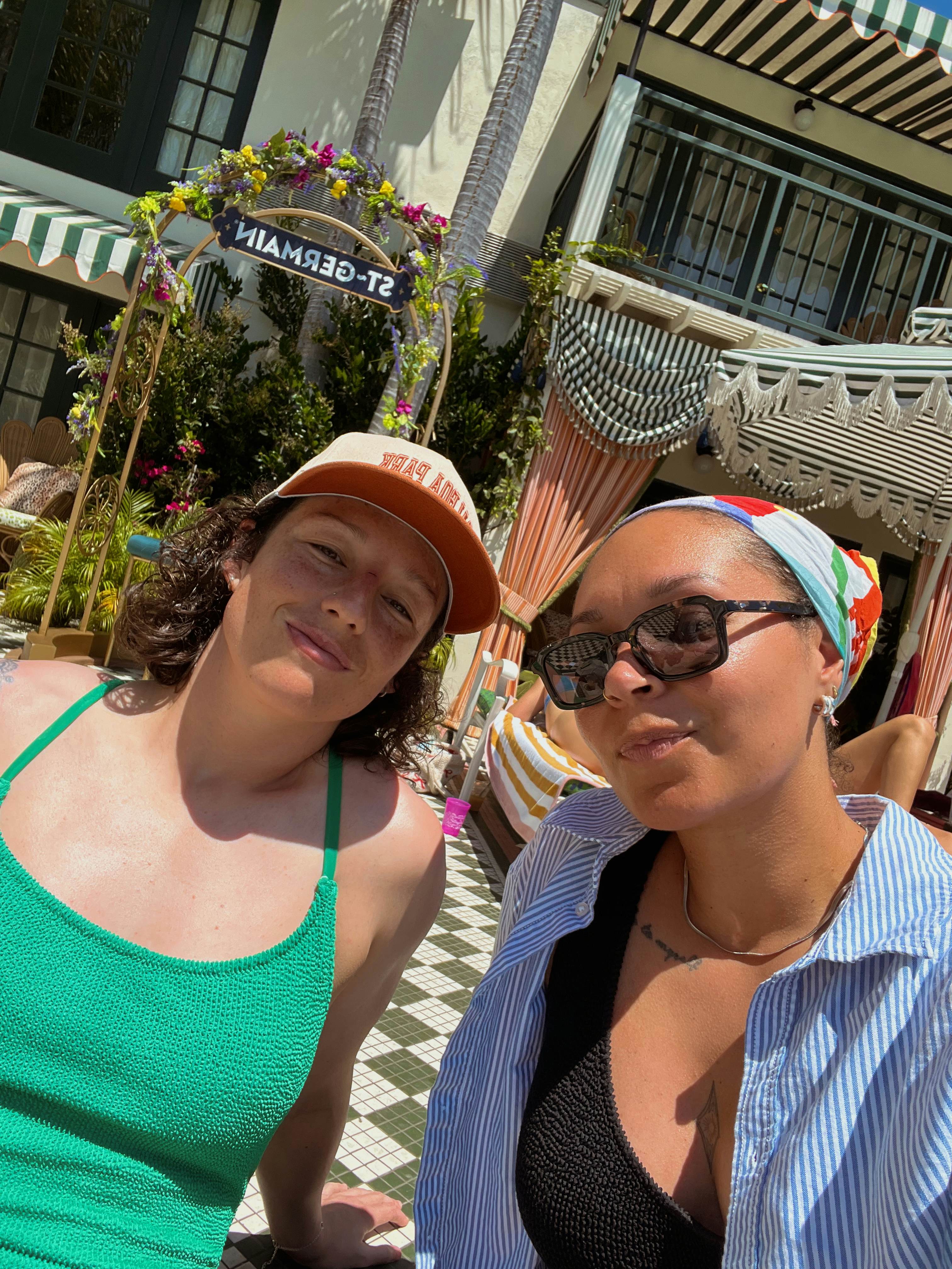 A selfie of two women smiling poolside on a sunny day.