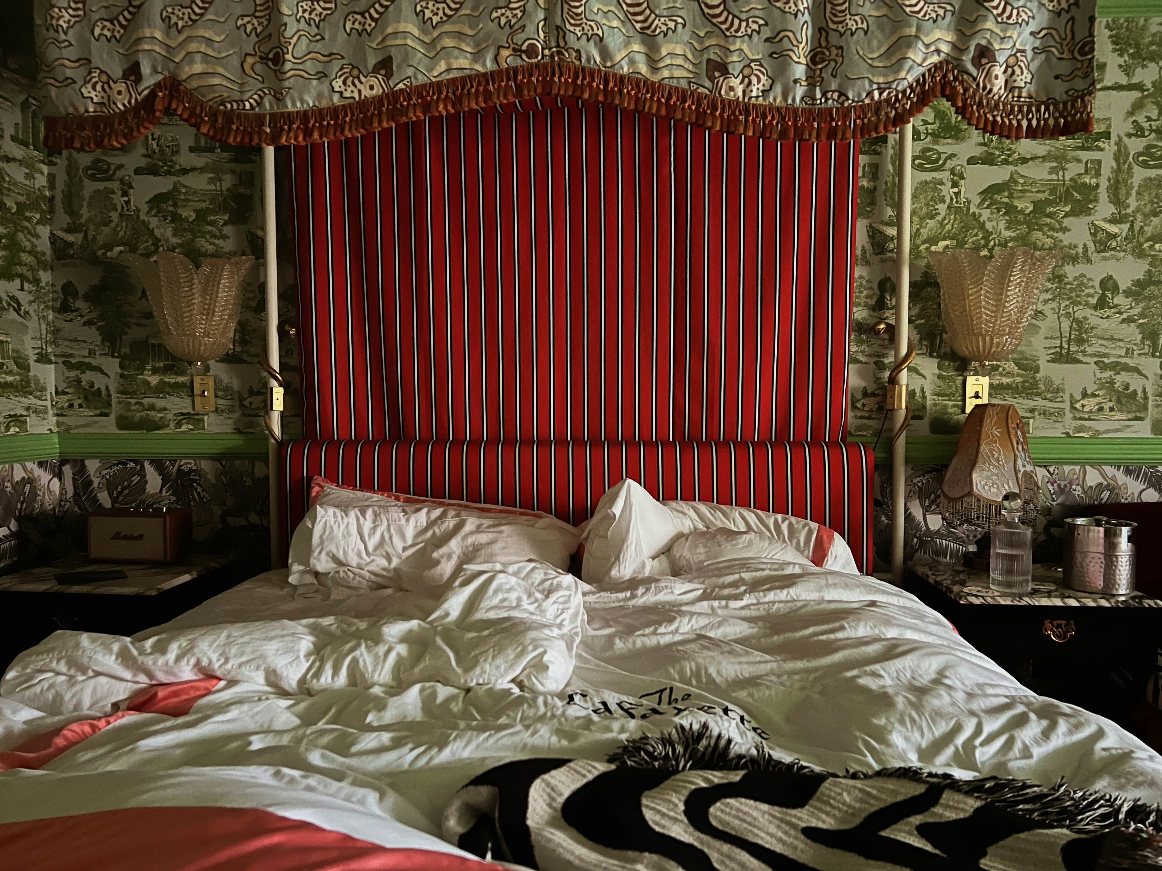 A rumpled bed of white sheets with red-and-white-striped headboard.