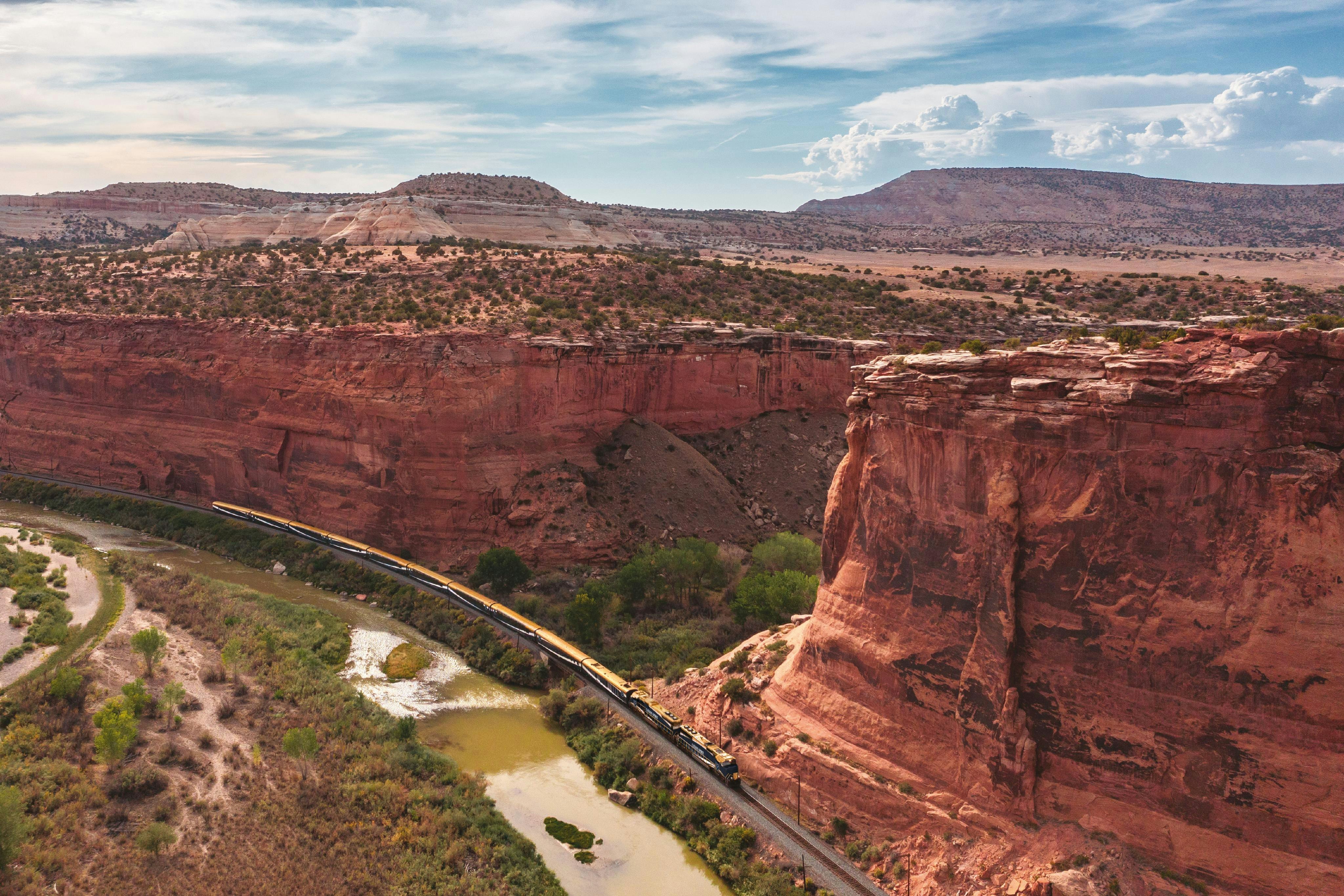 Aerial view of a train traveling in a canyon below red steppe mountains.