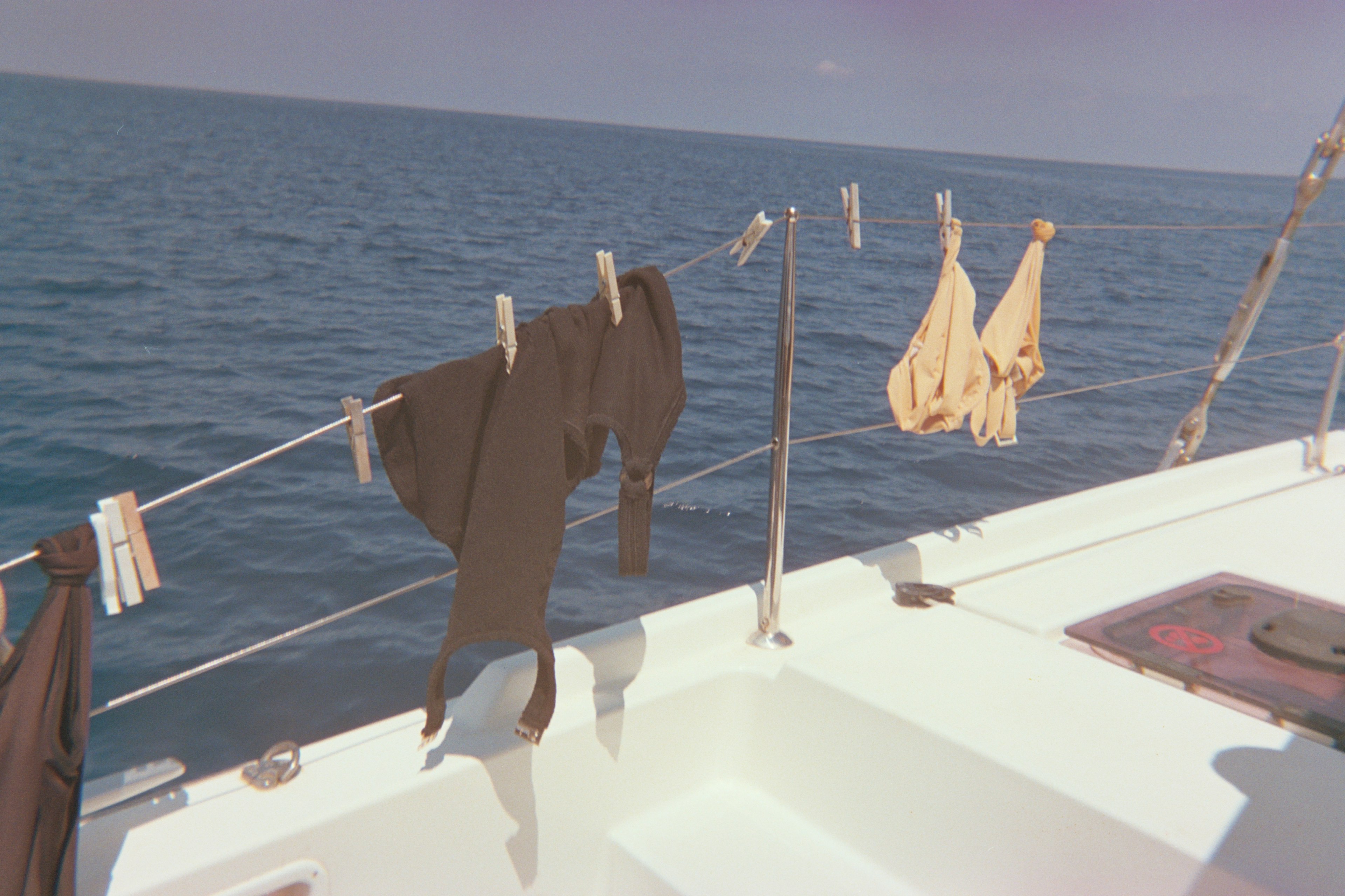 Swimsuits drying with clothespins on the guard ropes of a sailboat with the ocean behind them