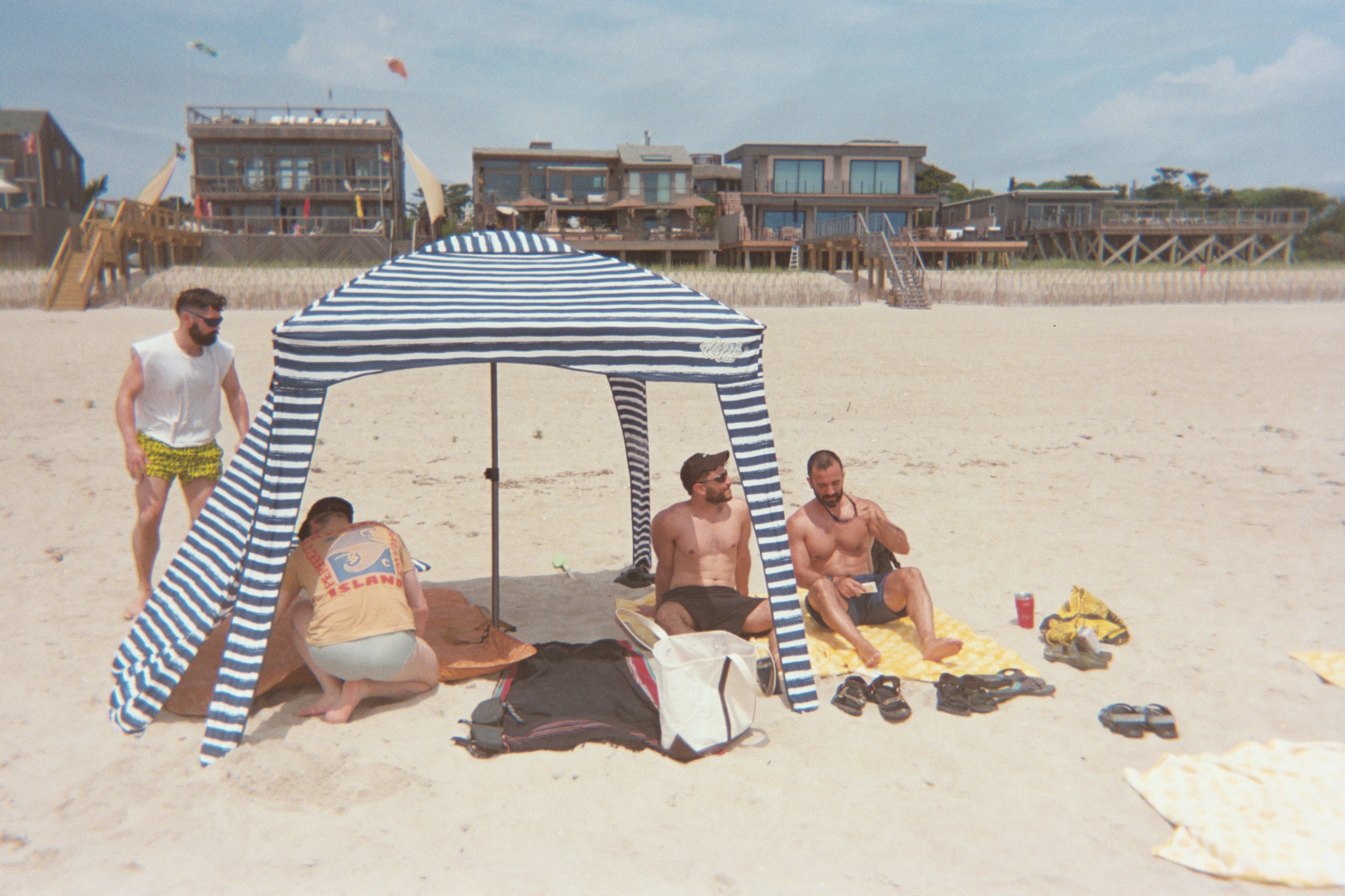 Four men sitting under a small canopy on the beach at Fire Island, New York