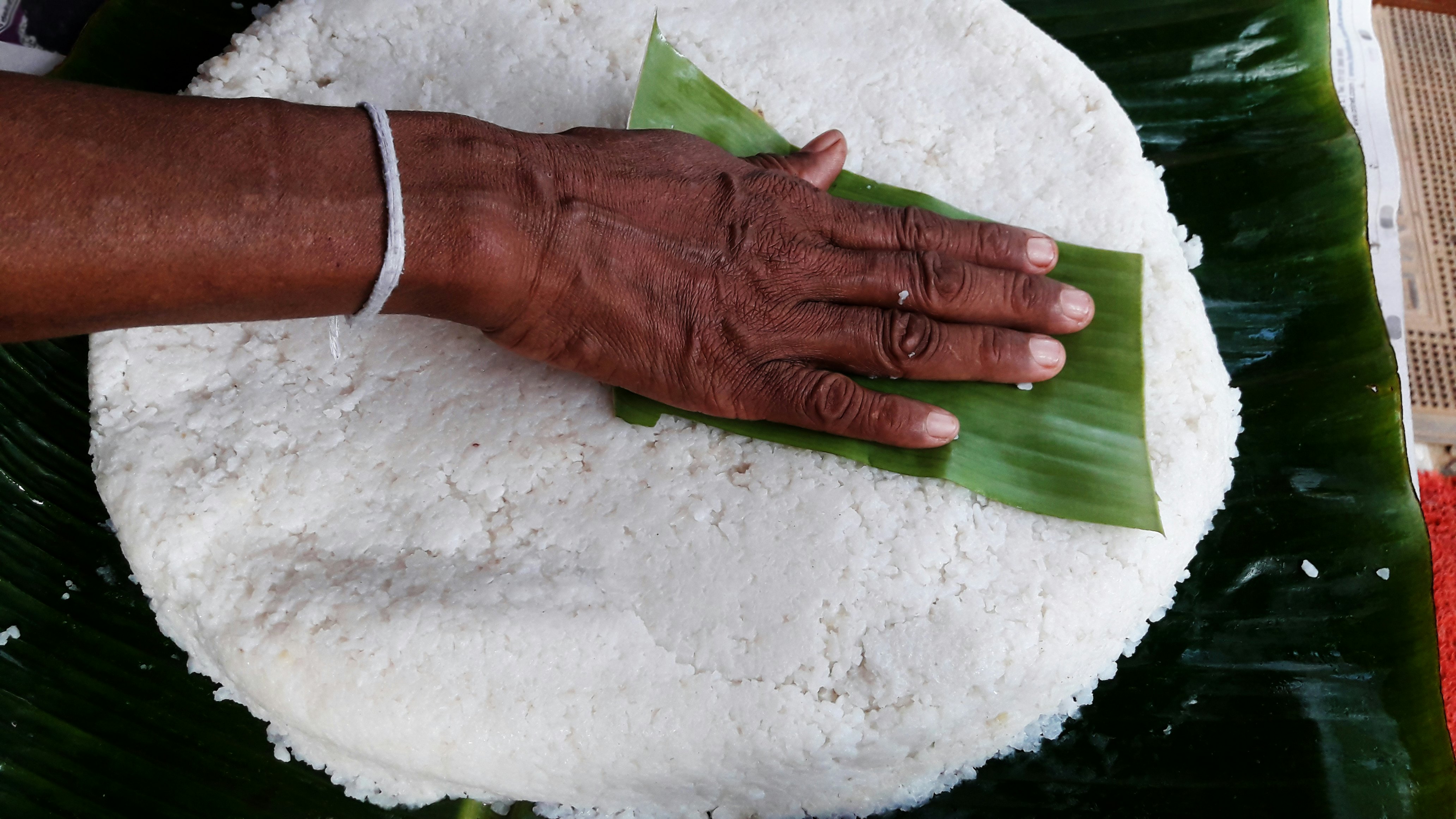 A hand places a banana leaf on kiribath.