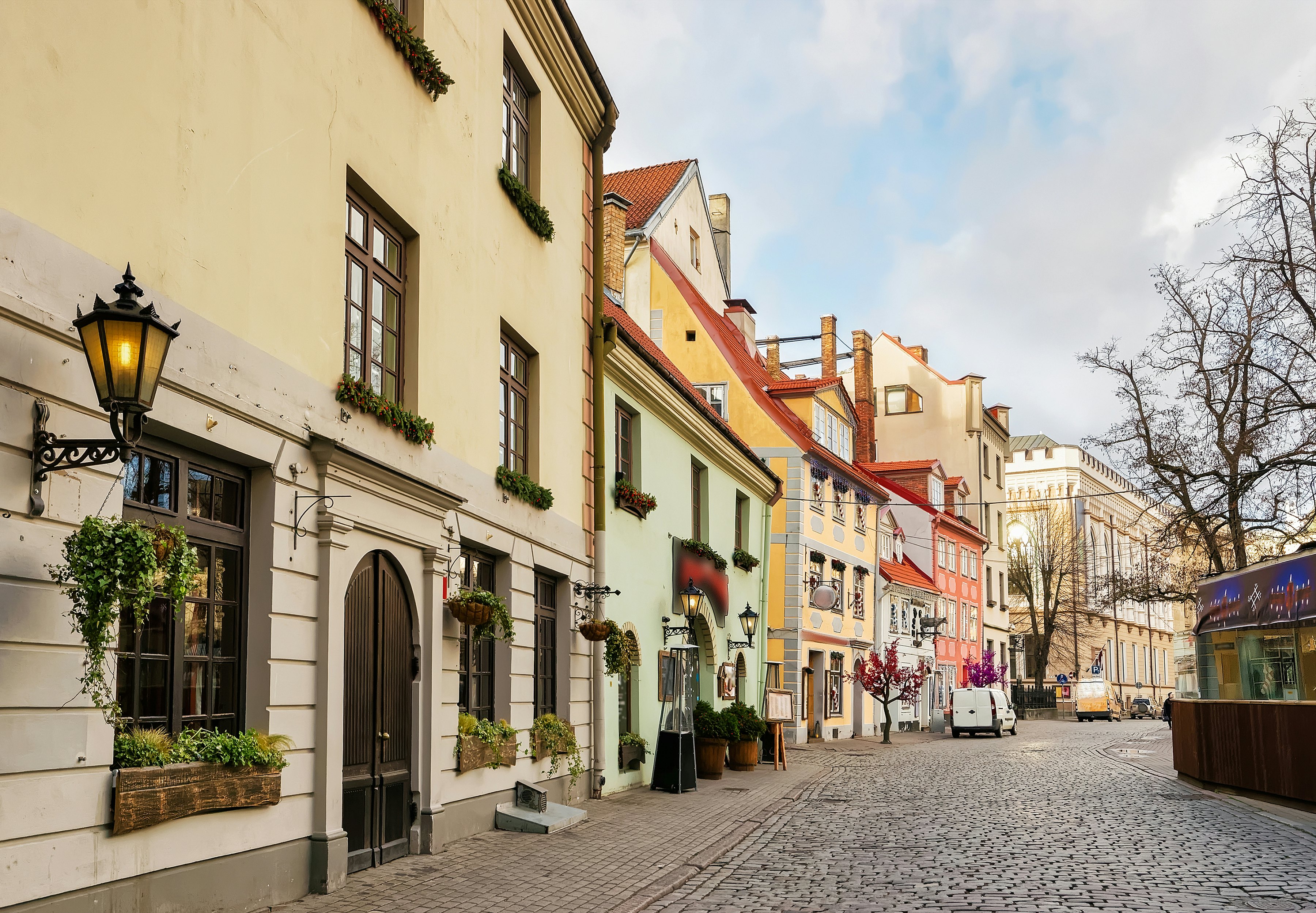 View down a cobblestone street with colorful stone homes to the left on an overcast day.