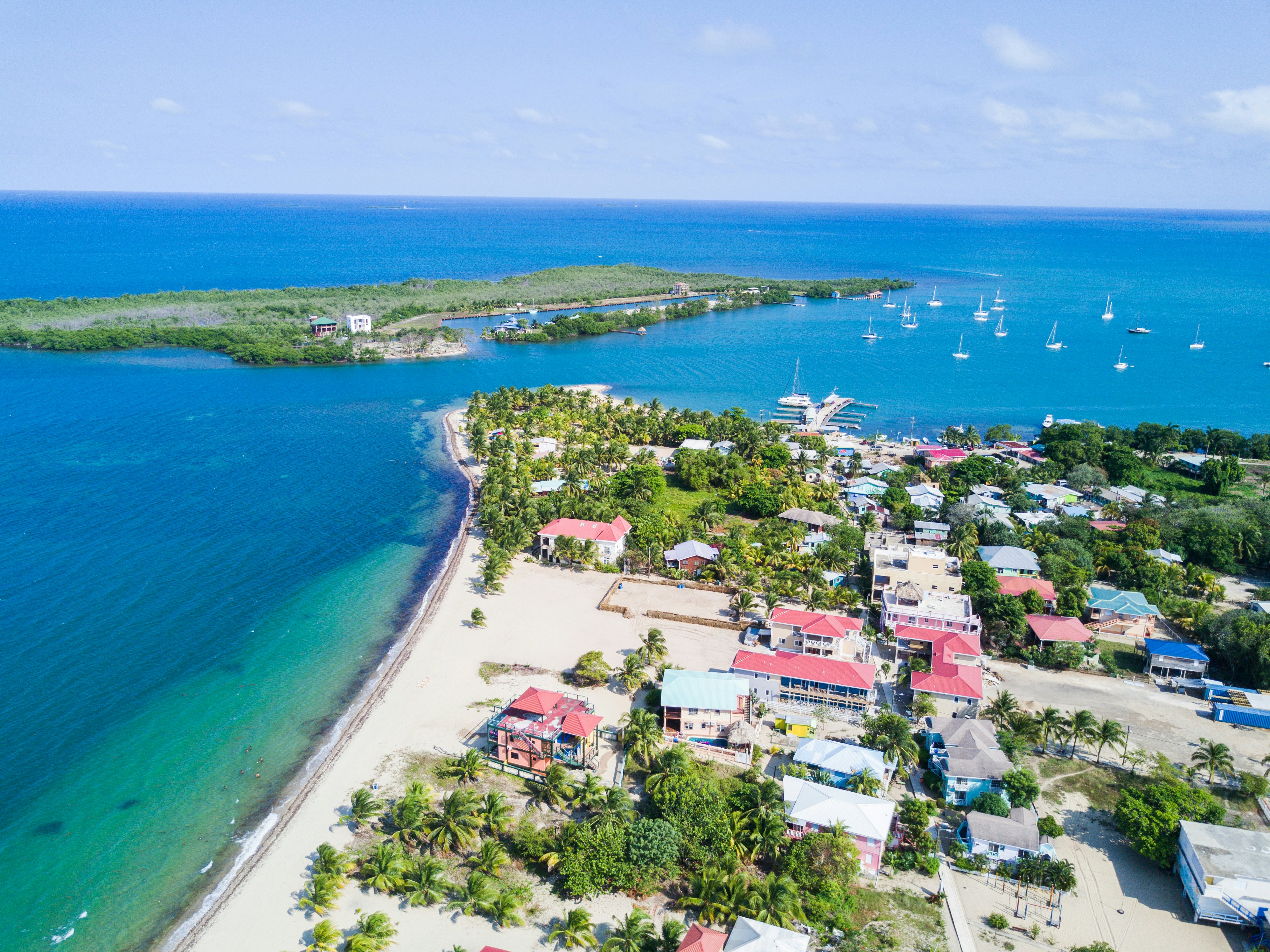 Aerial view of Placencia in Southern Belize, with pink, blue and white rooftops, and white boats on the blue wayer