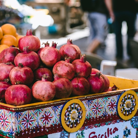 Ripe pomegranates in a brightly colored bin at an outdoor market.