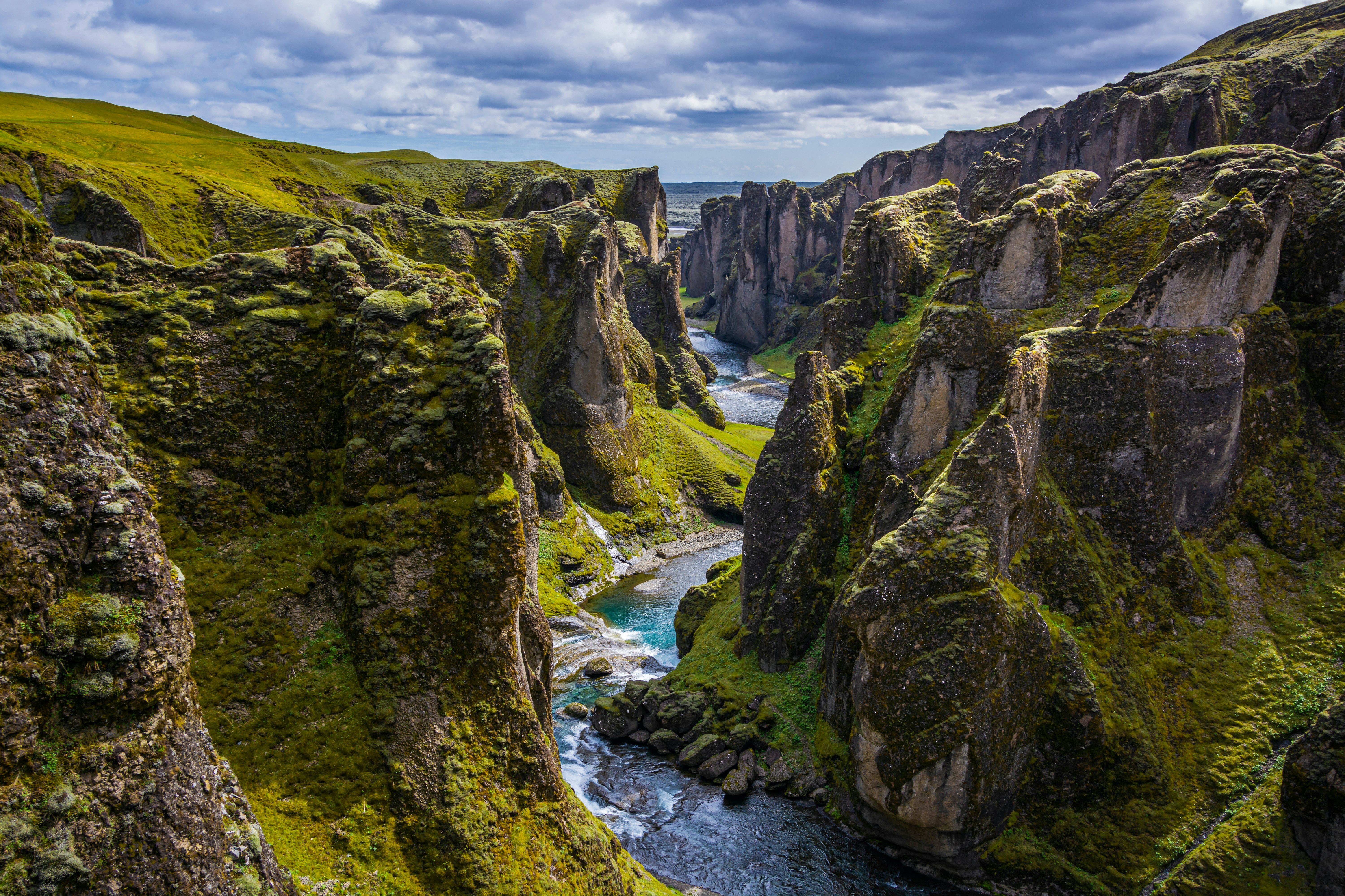 A steep canyon with green moss growing on the rock has water running through it.