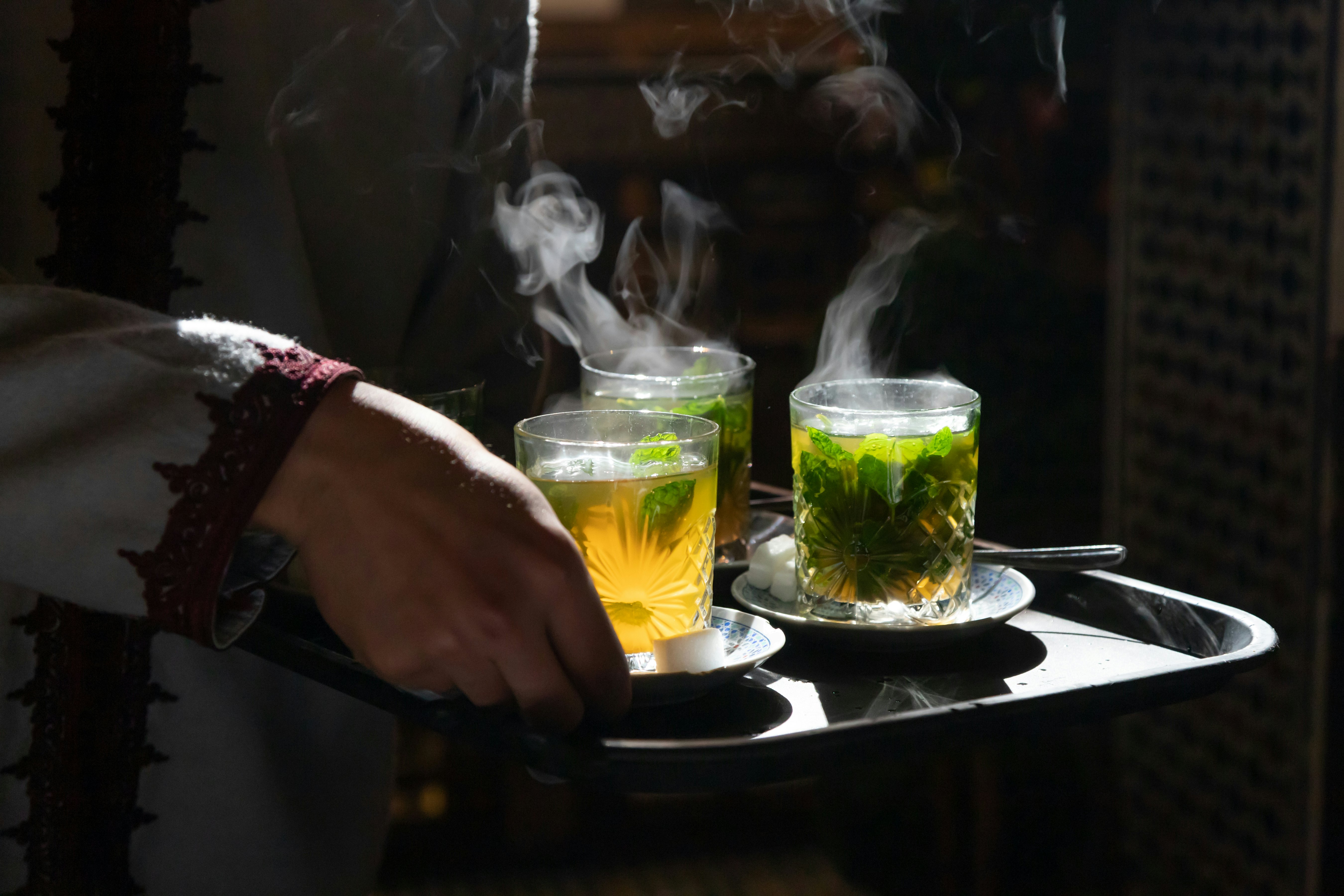 Traditional mint tea in glasses steaming backlit by sun being served on tray