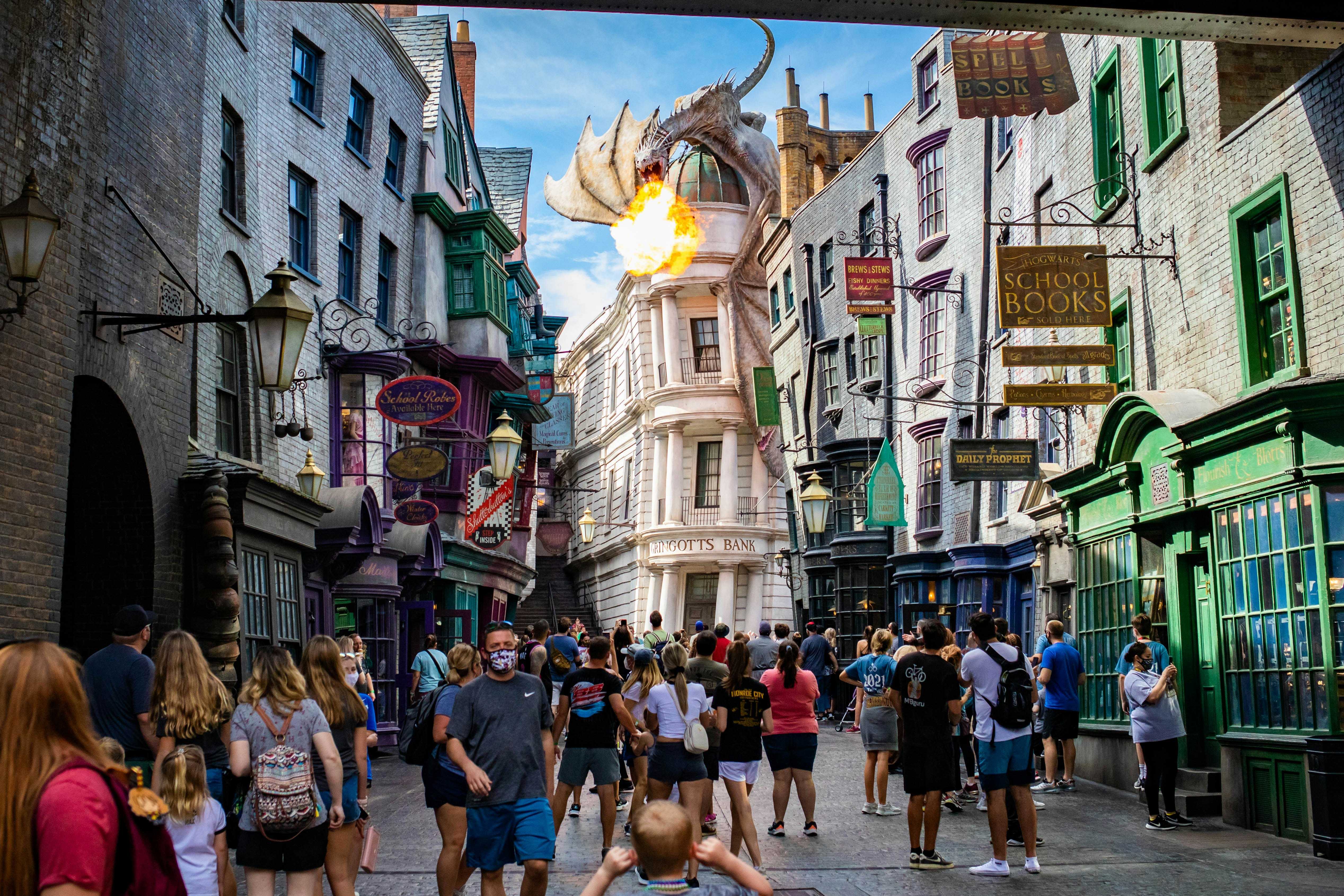 A crowd of people wanders an elaborately constructed environment depicting a town street, with an animatronic dragon breathing fire above them.