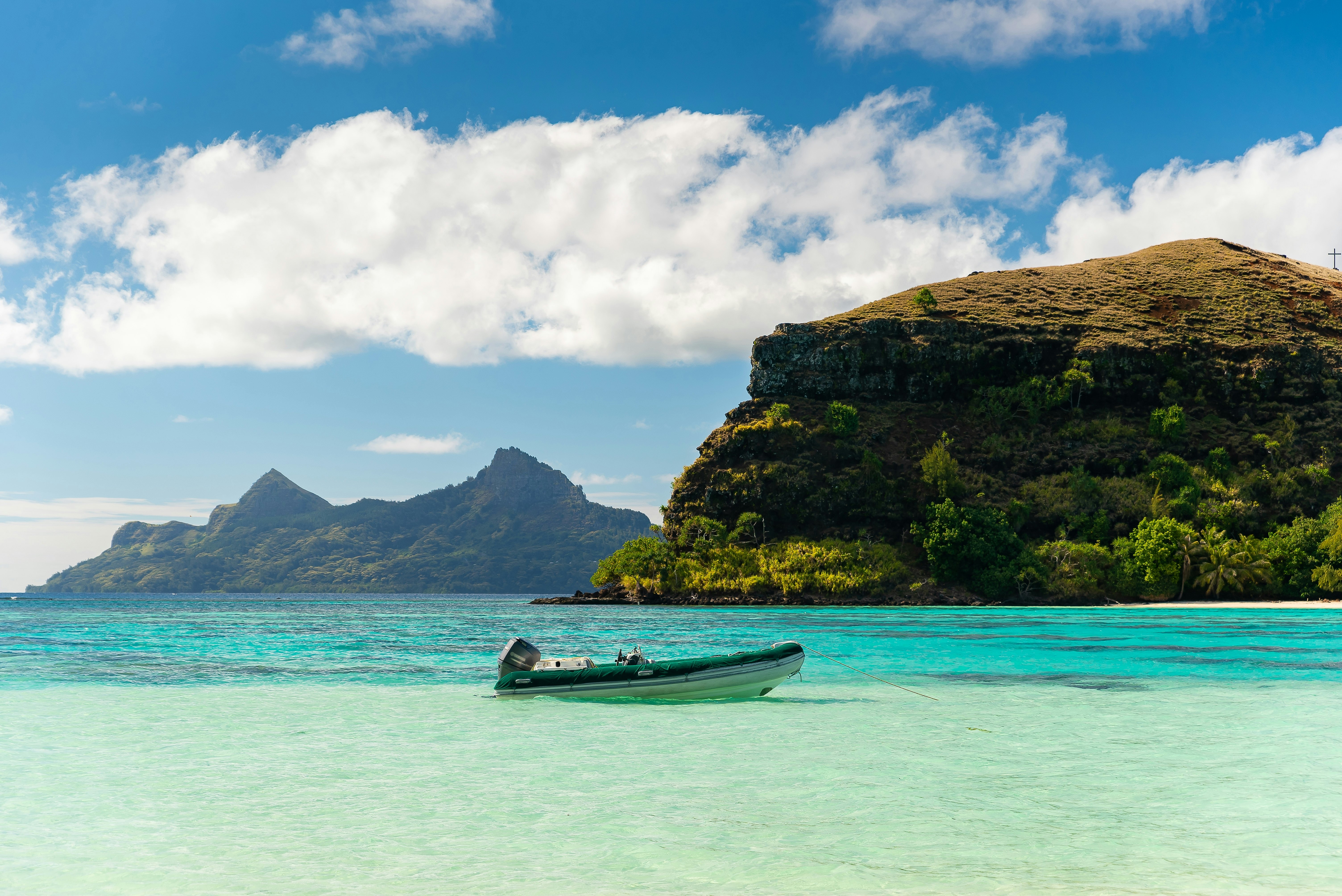 A small motor boat moored in the shallows of a hilly island.