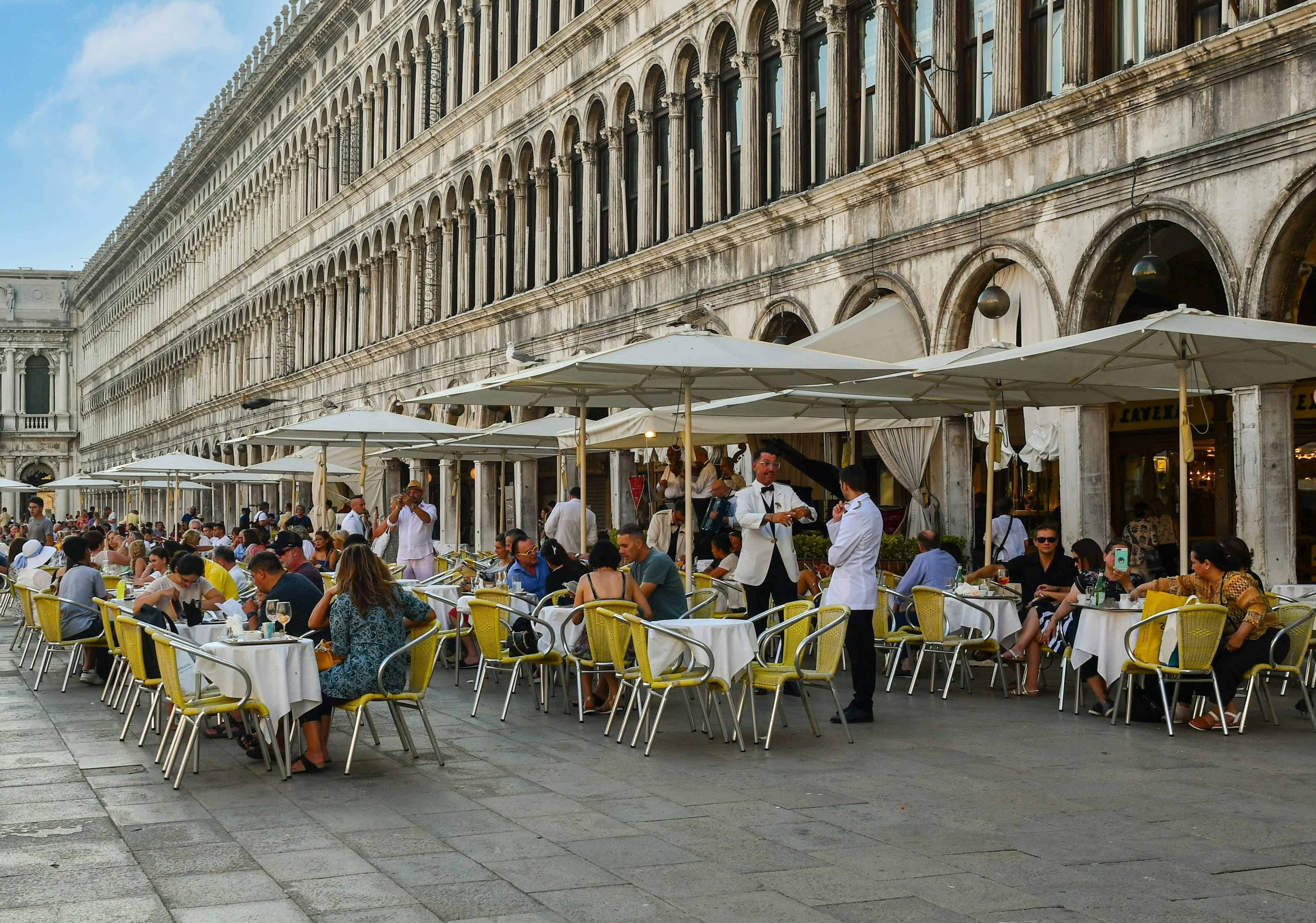 People sitting at outdoor tables under umbrellas in Piazza San Marco in Venice.