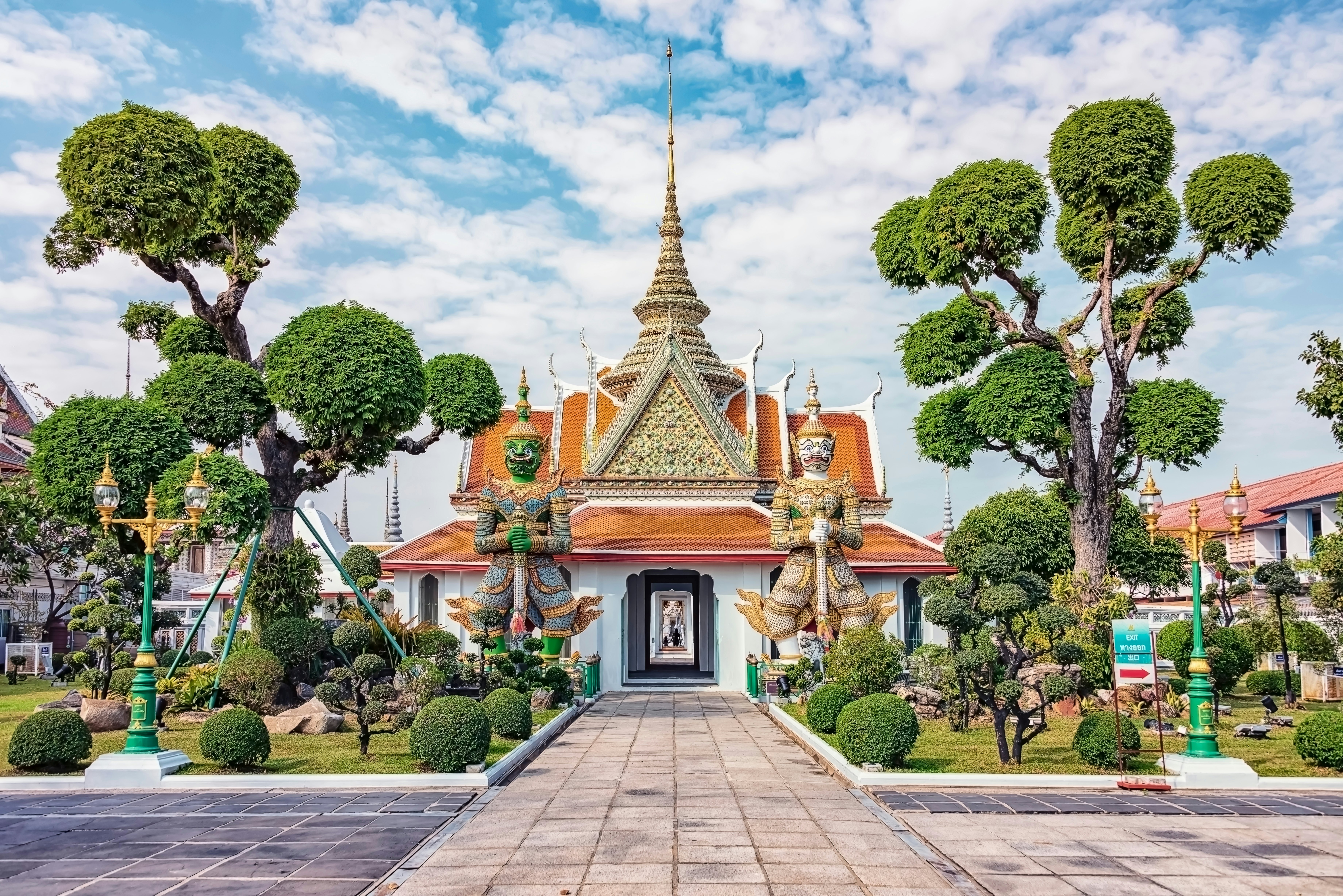 Guardian statues at Wat Arun in Bangkok, Thailand, flanked by rounded trees.