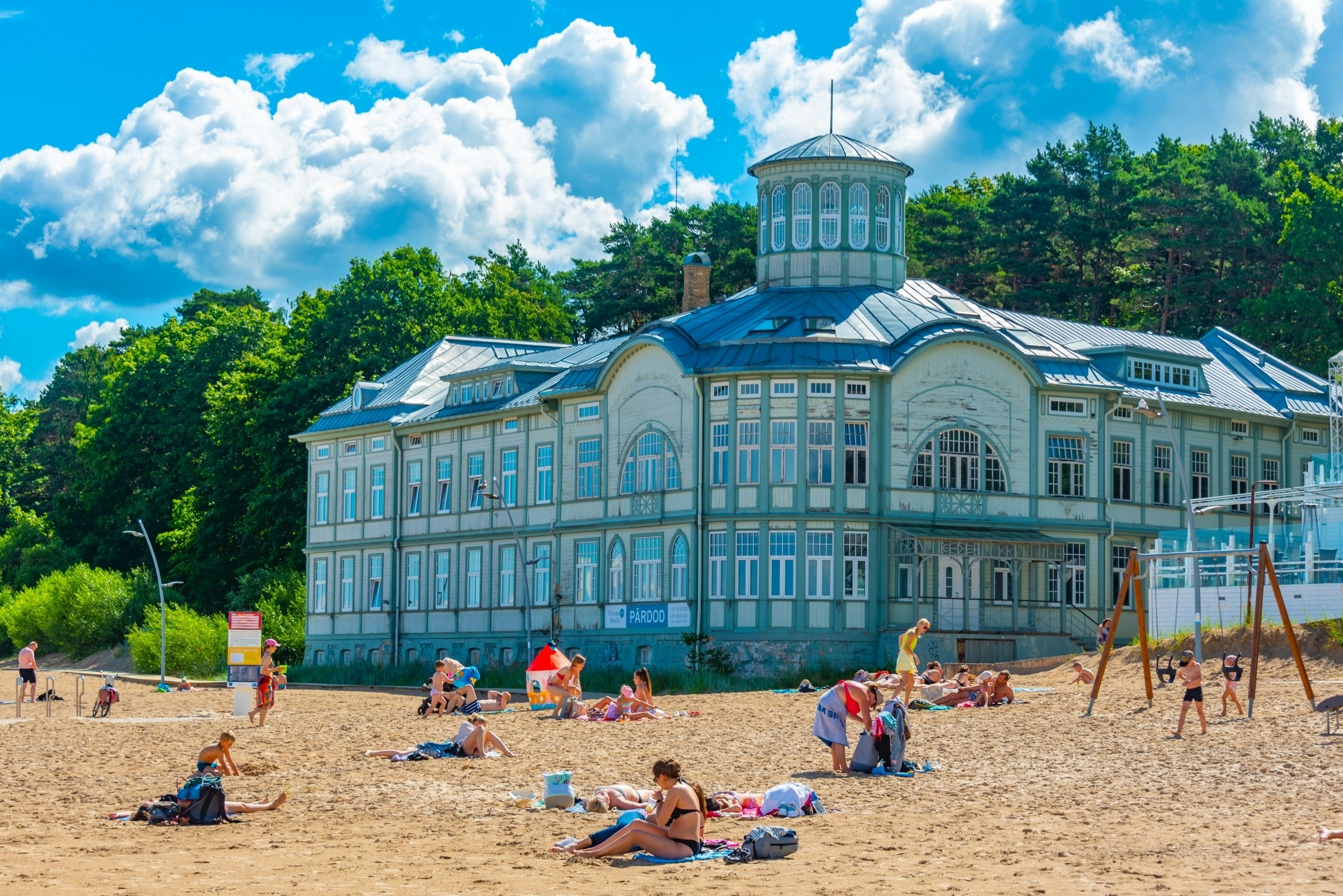People play on a sandy beach overlooked by an art deco villa.