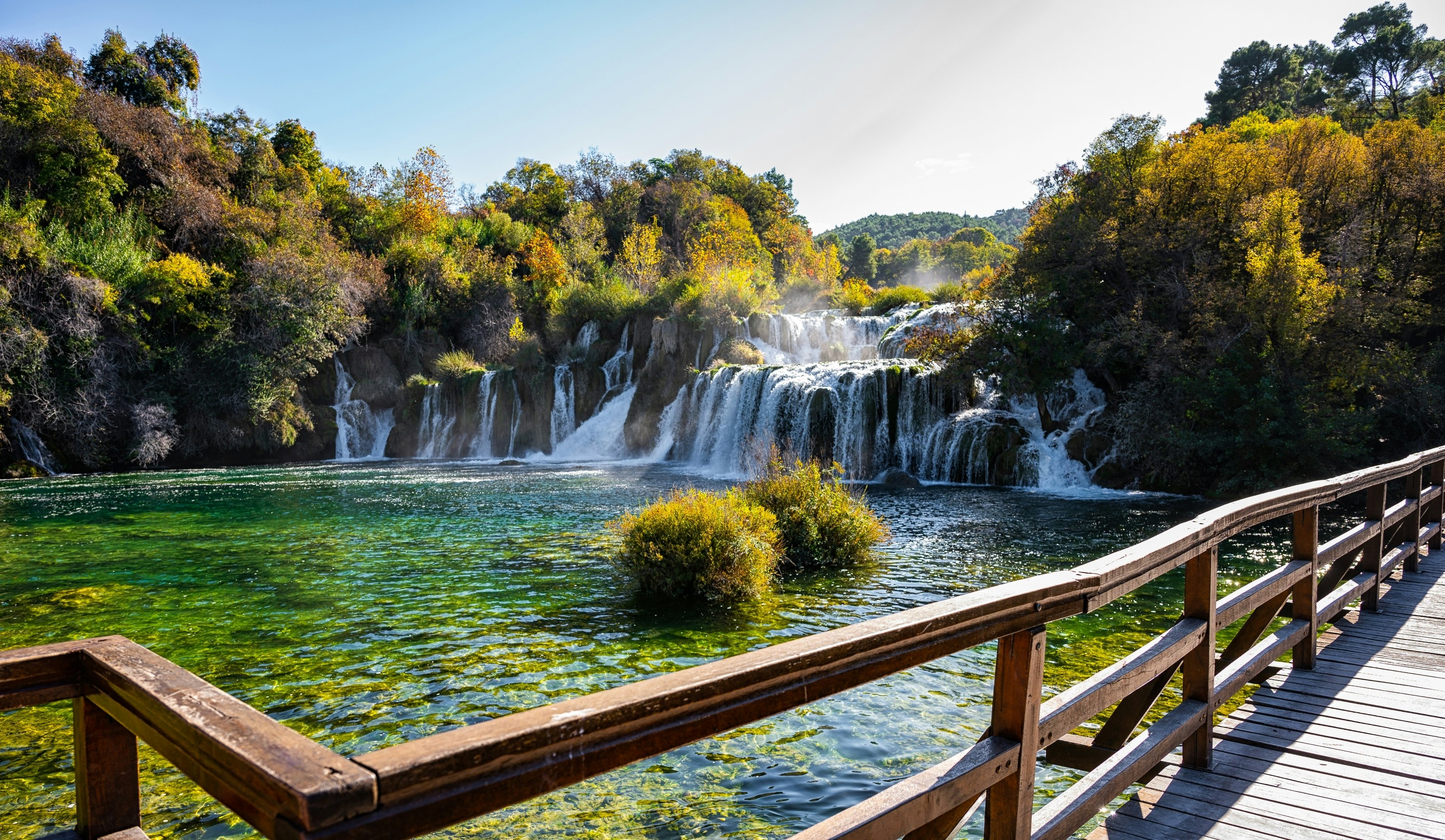 Trees and waterfalls in Krka National Park, with a fenced wooden bridge in the foreground