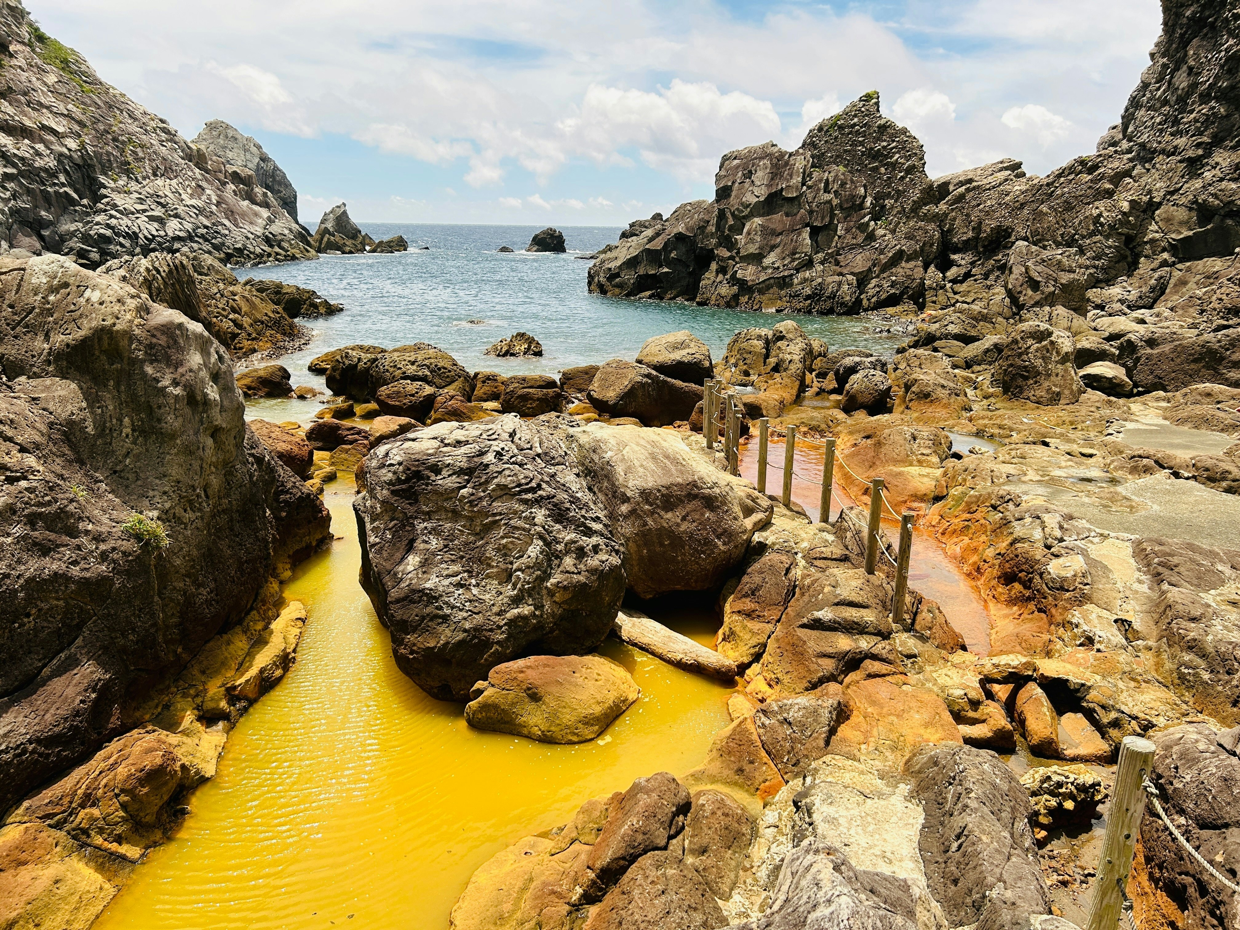 A natural hot spring beside the ocean. A pathway leads to the shore. The water in the spring is colored yellow by iron.