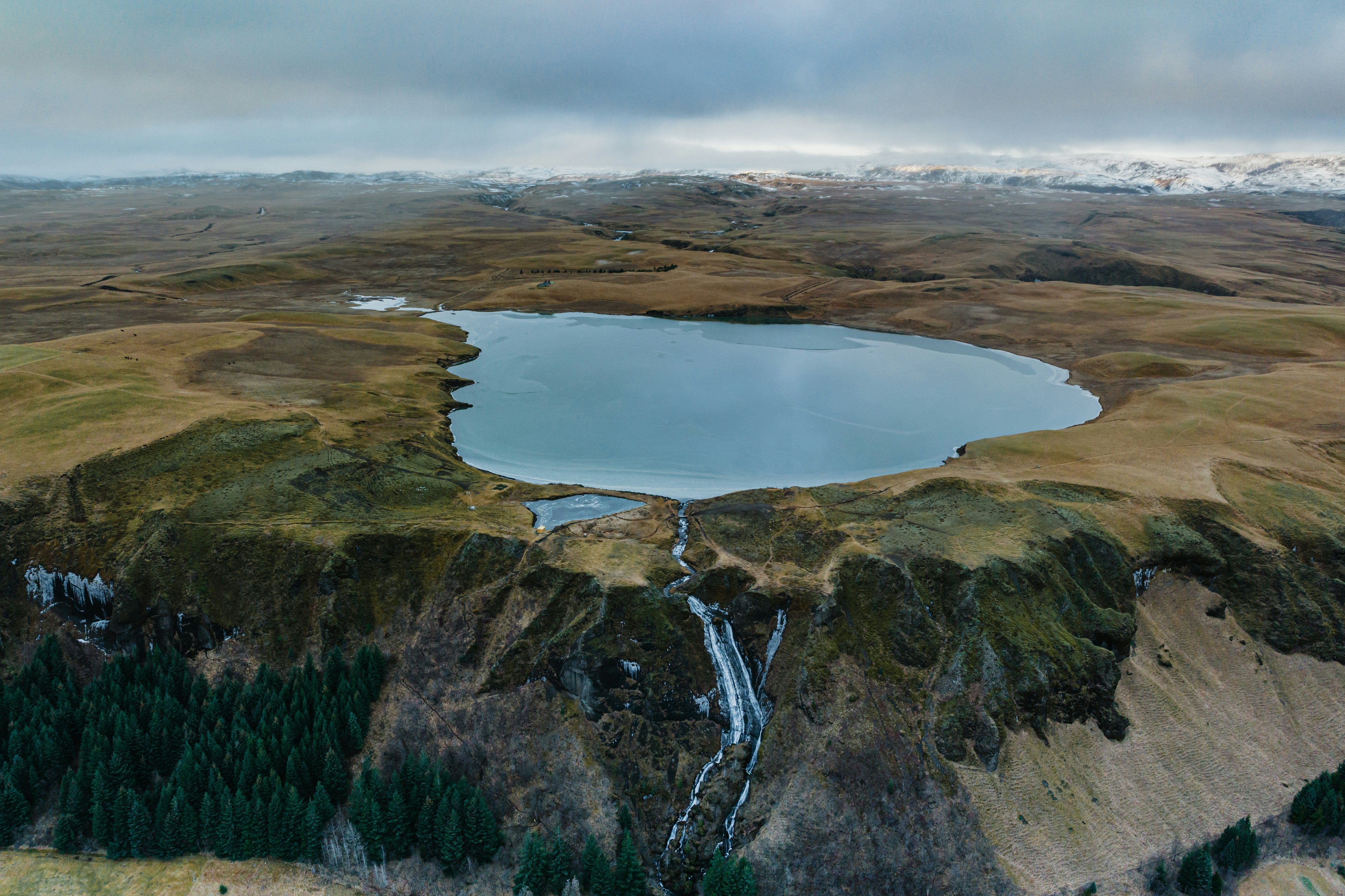 A placid blue lake in a barren landscape in Iceland sits above a steep drop-off.