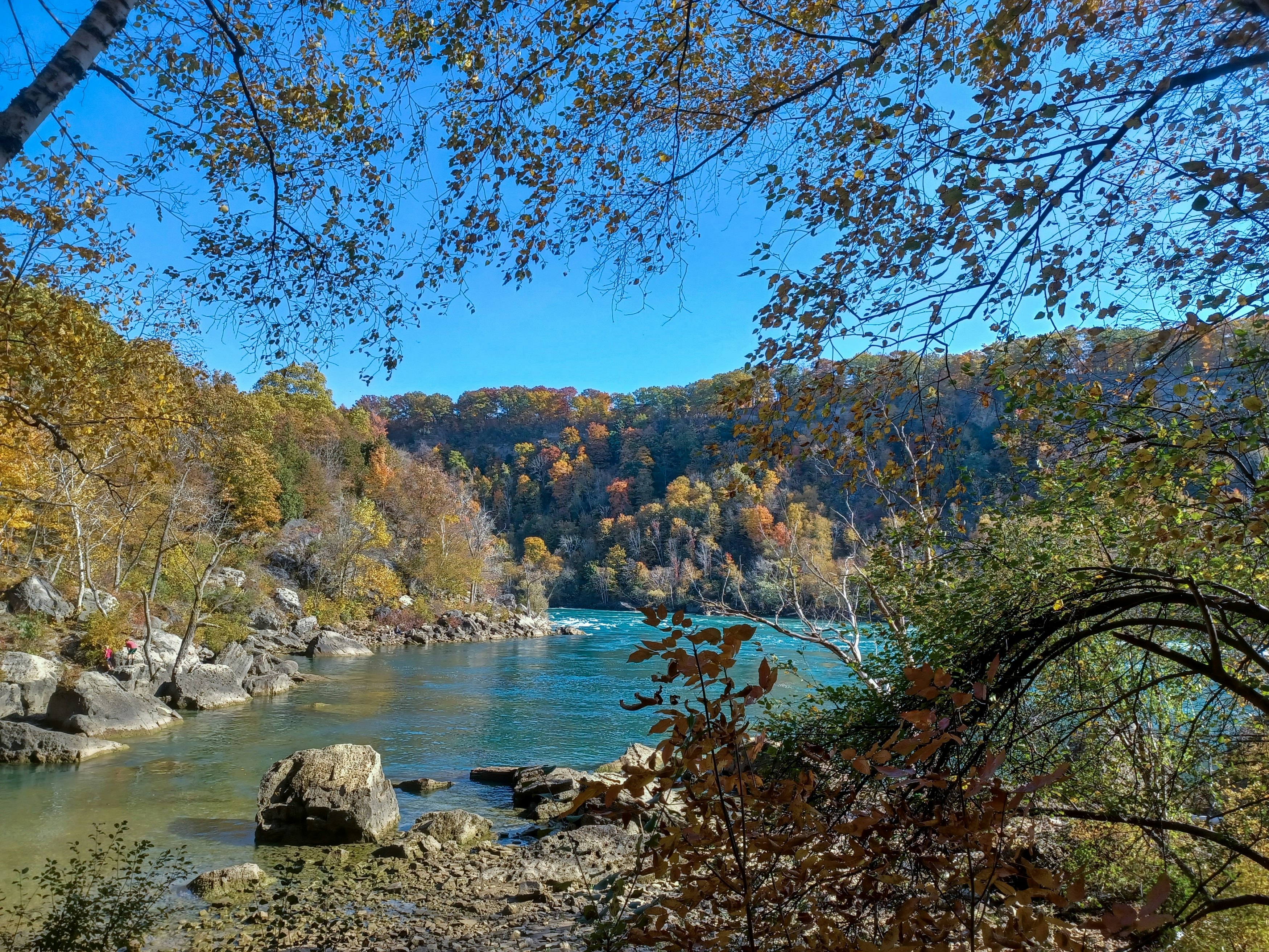 A bend in a turquoise-colored river in Ontario, Canada, is seen from a rocky shore in autumn.