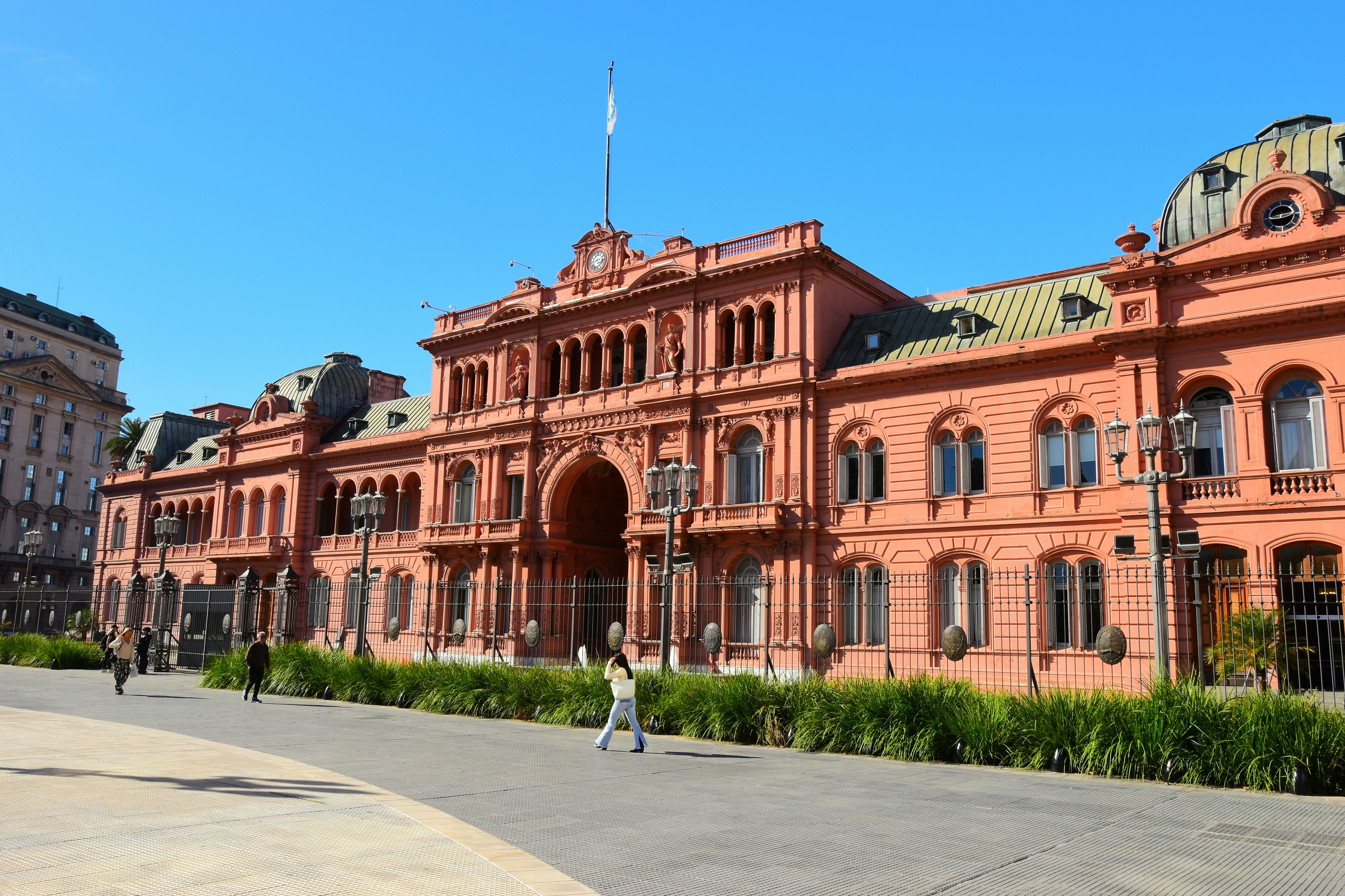 Pedestrians in front of the bright pink Casa Rosada on a blue-sky day