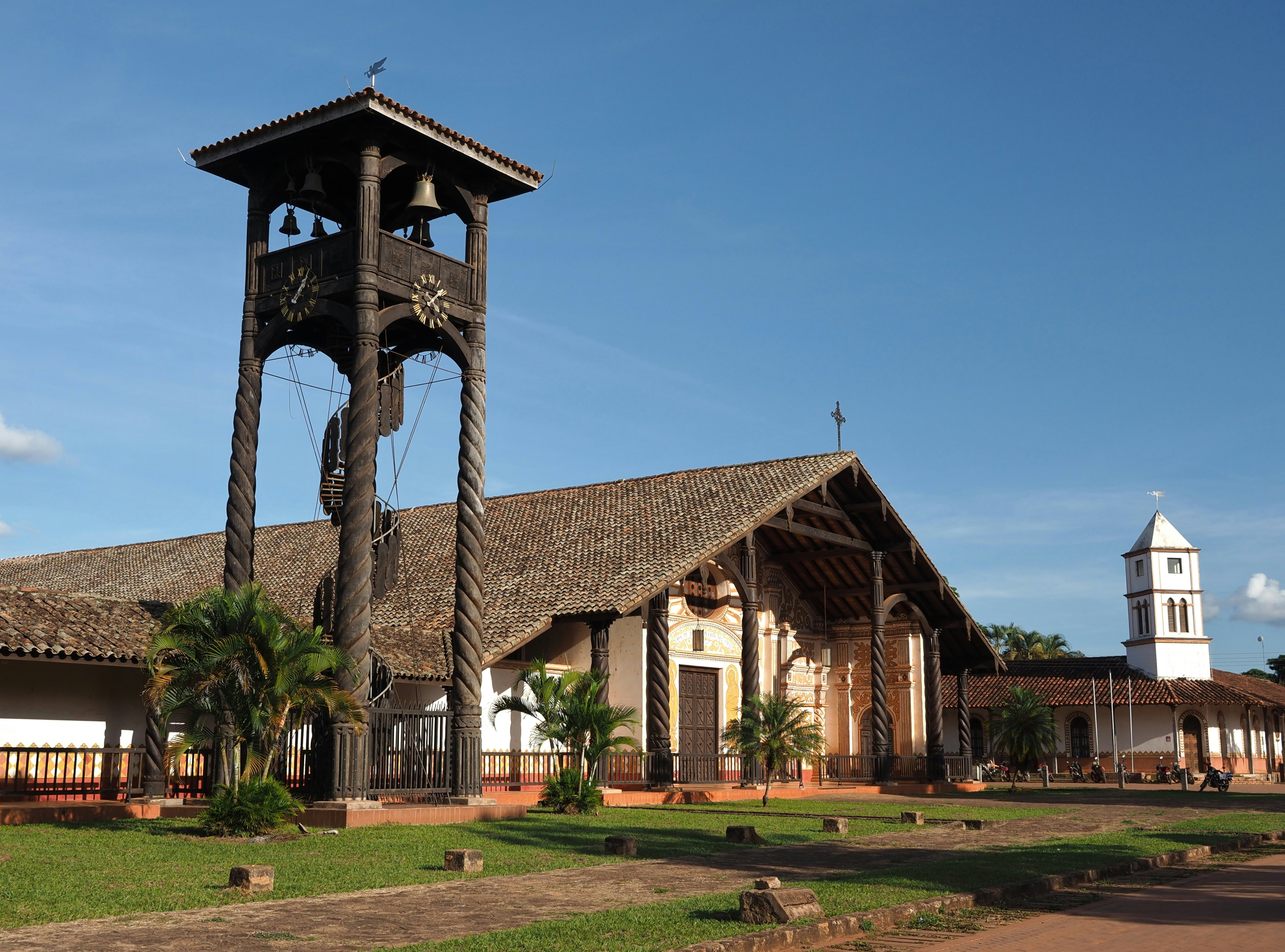An ancient church with an ornate facade stands near a wooden bell tower and clock.